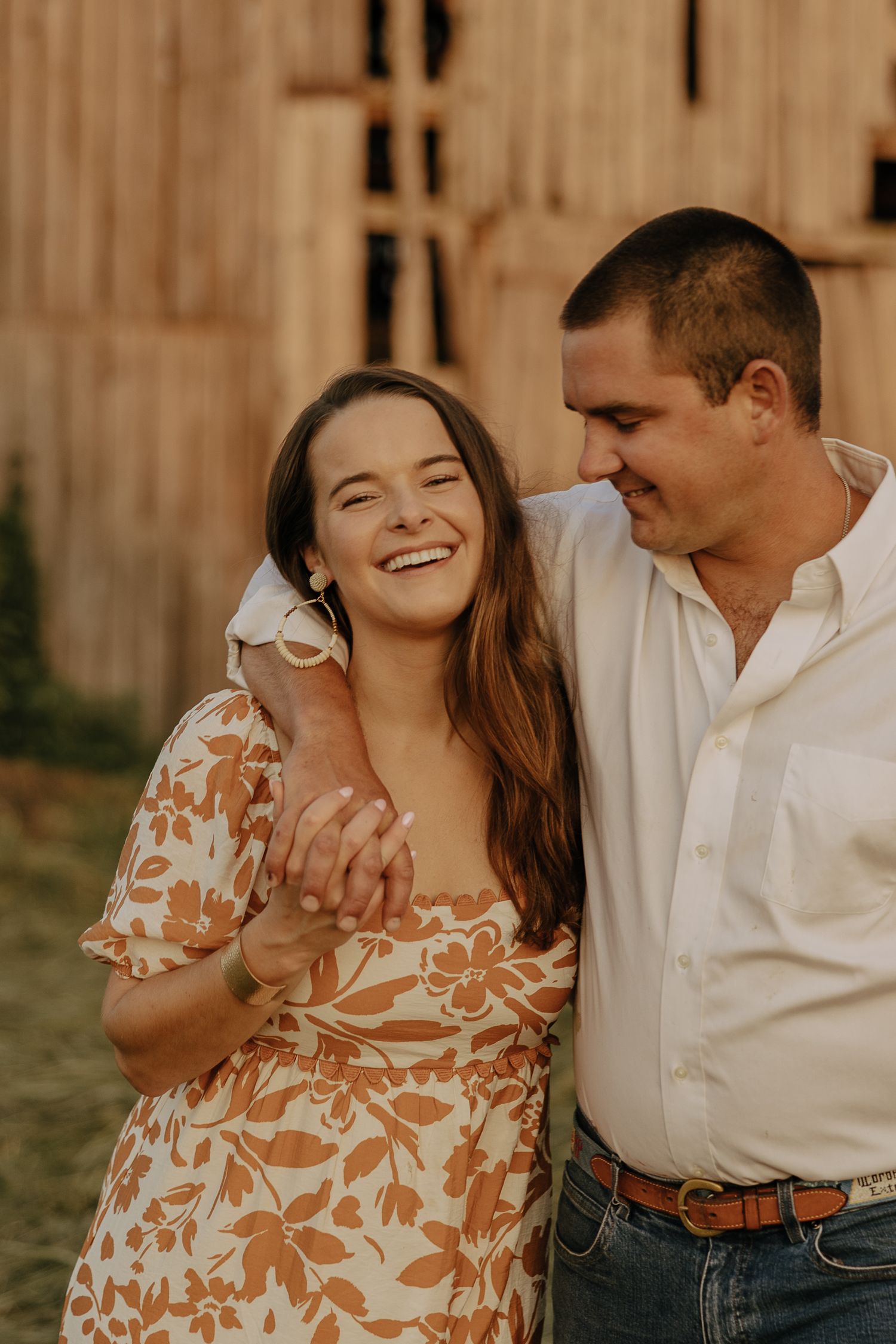 Intimate moment between couple in casual attire against wooden barn backdrop.