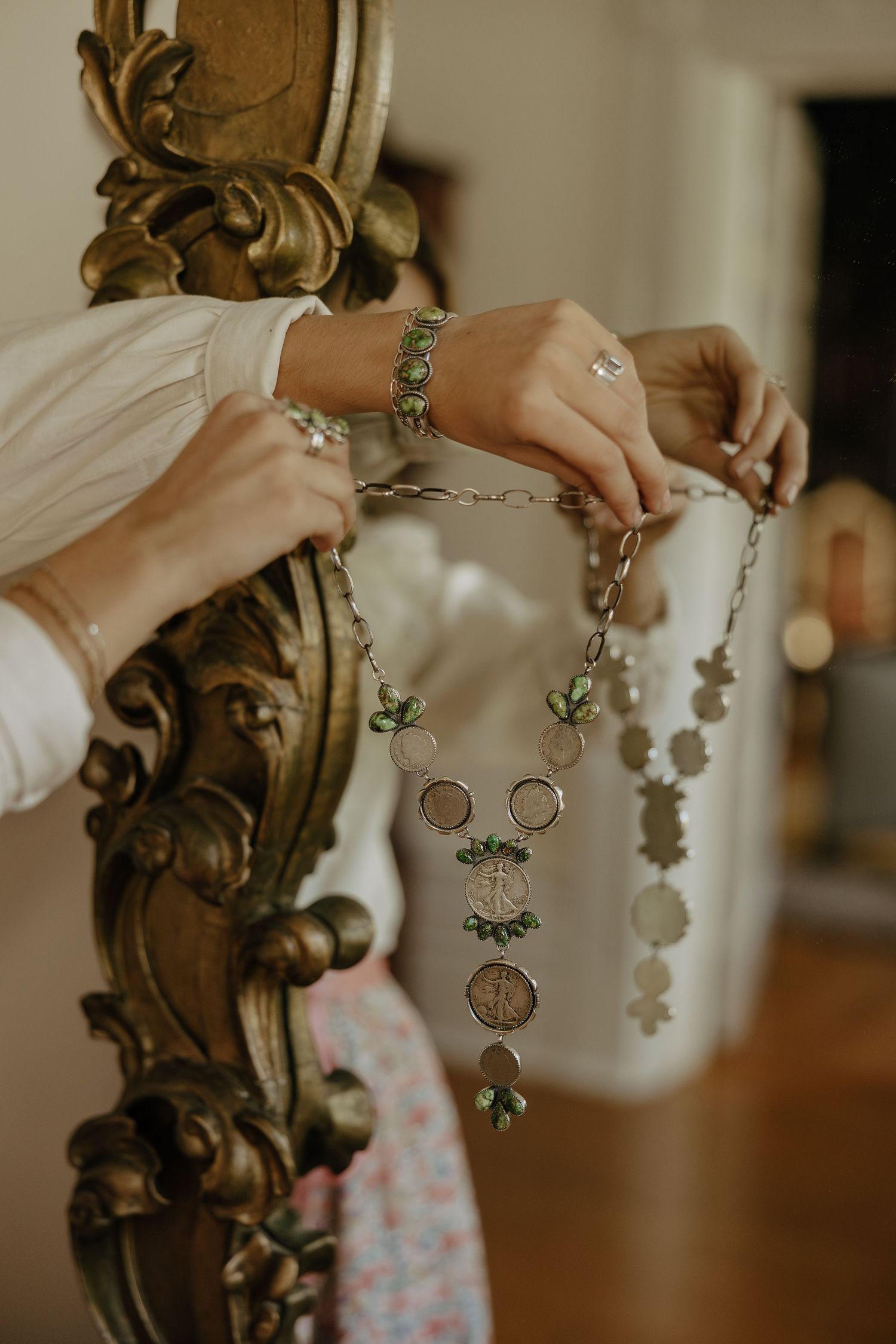 Close-up of hands holding vintage-style jewelry and accessories against an ornate gold mirror frame.