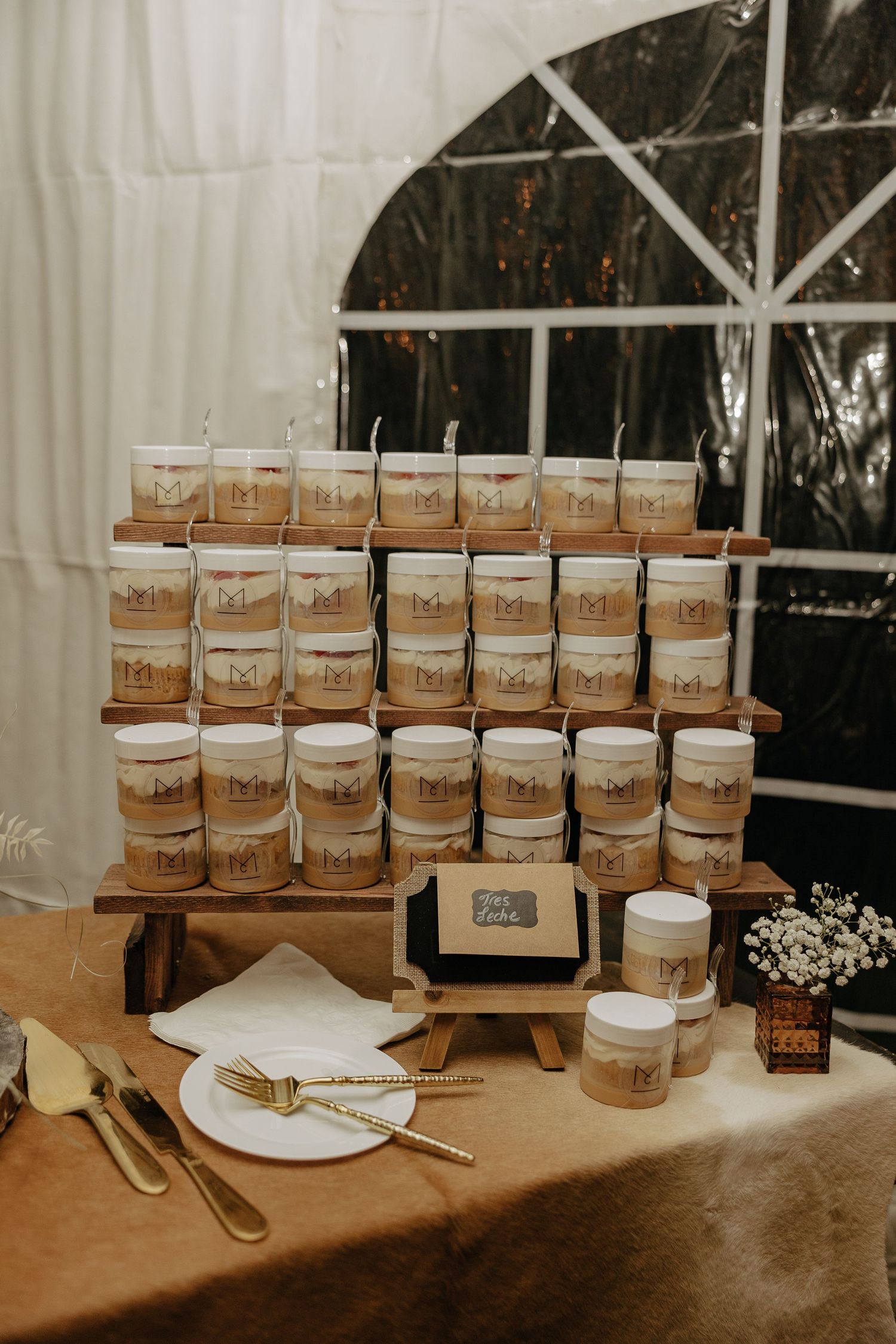 Wedding favor display featuring rows of small honey jars arranged on wooden stands with rustic white decor elements.