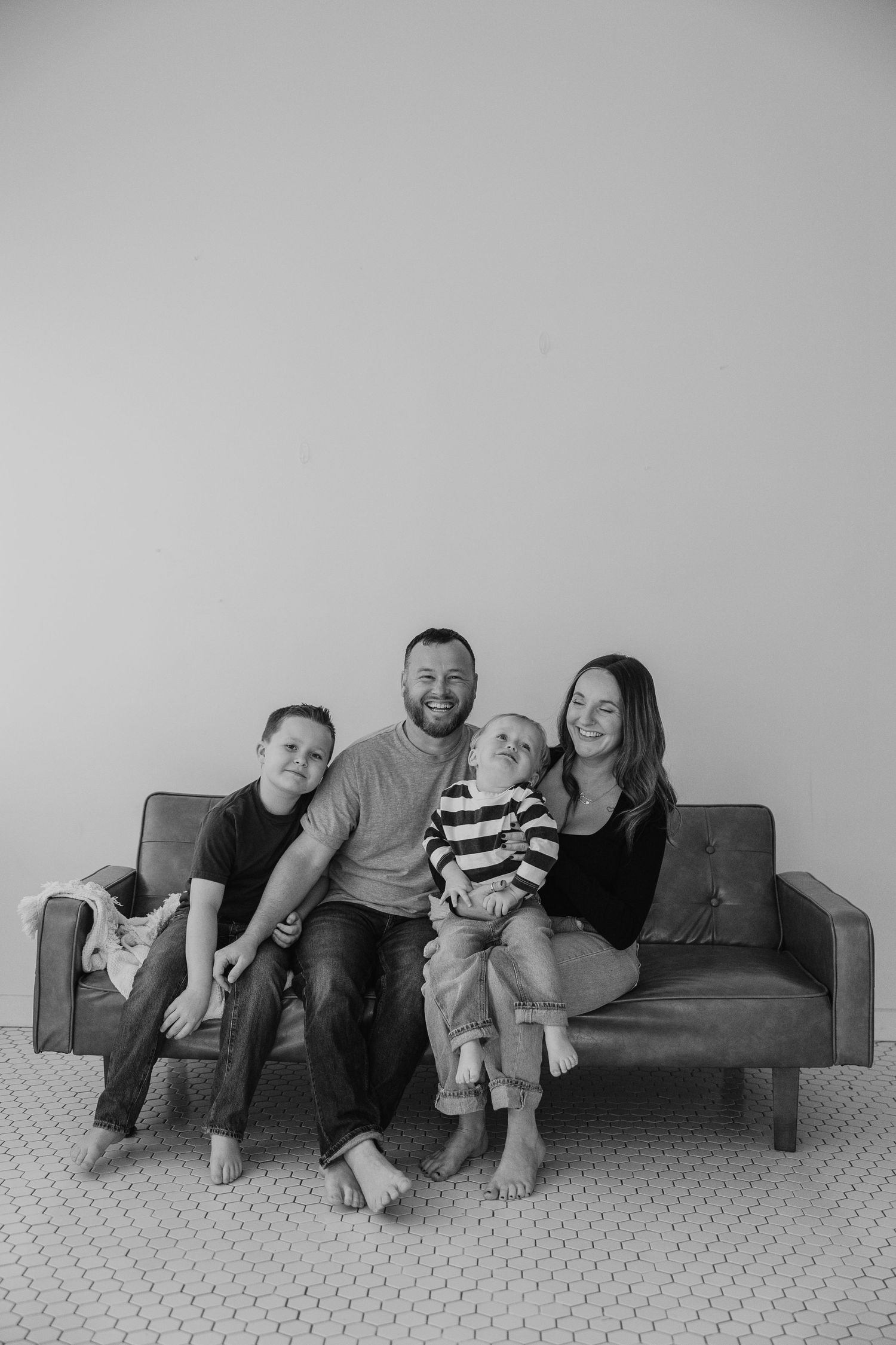 A sequence of black and white photos showing a family lounging together on a dark couch against a light background.