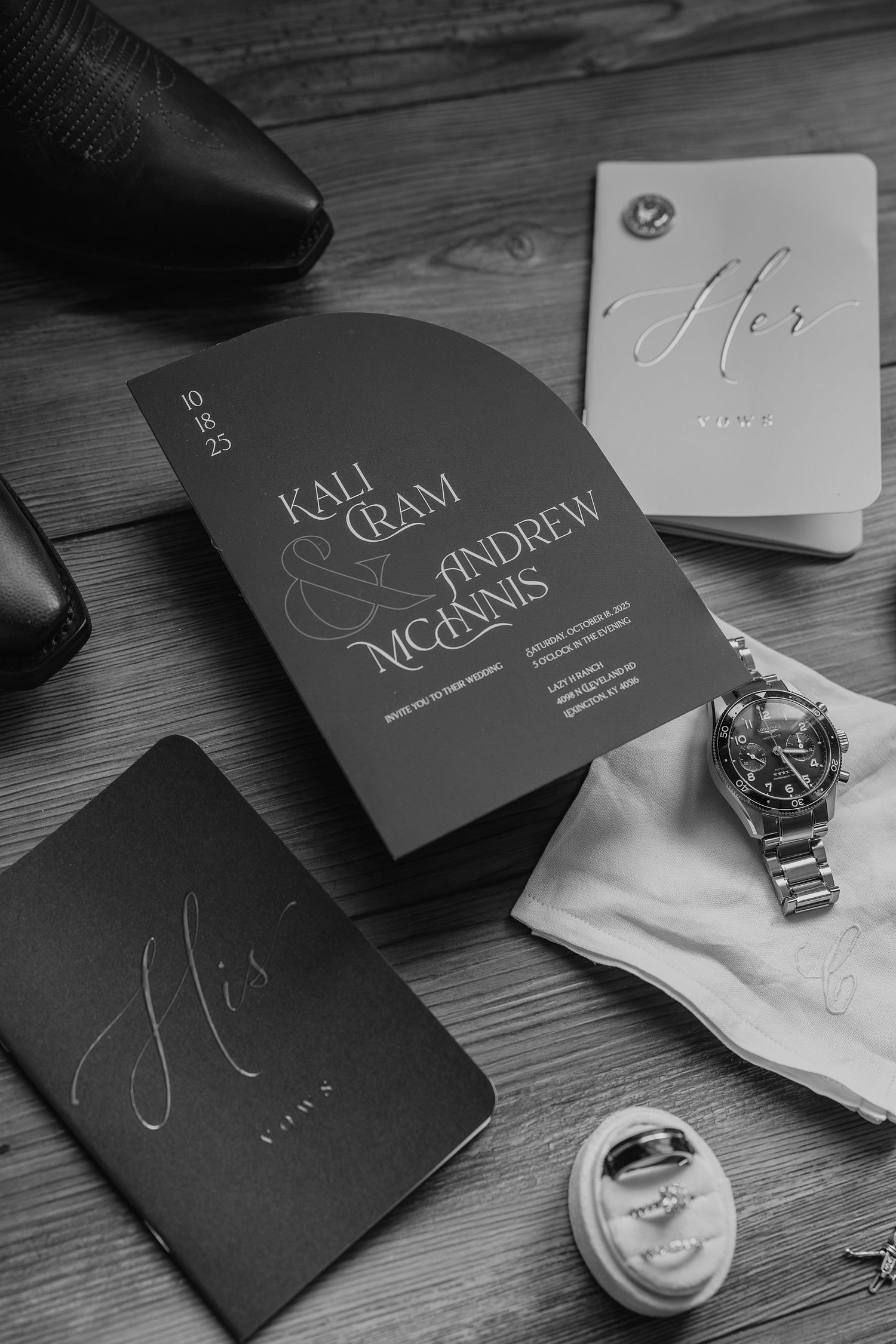 Elegant black and white wedding invitation with calligraphy alongside watch and accessories on wooden surface.