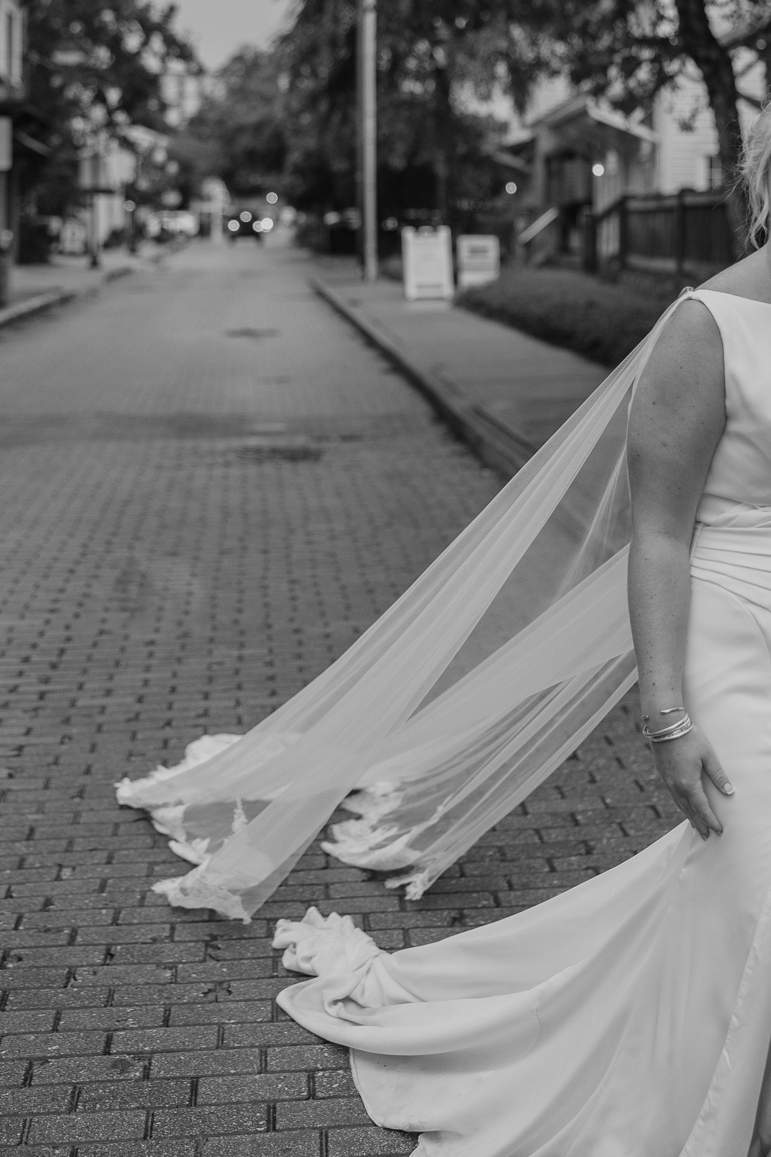 Flowing white wedding veil trailing across cobblestone street in black and white photography.