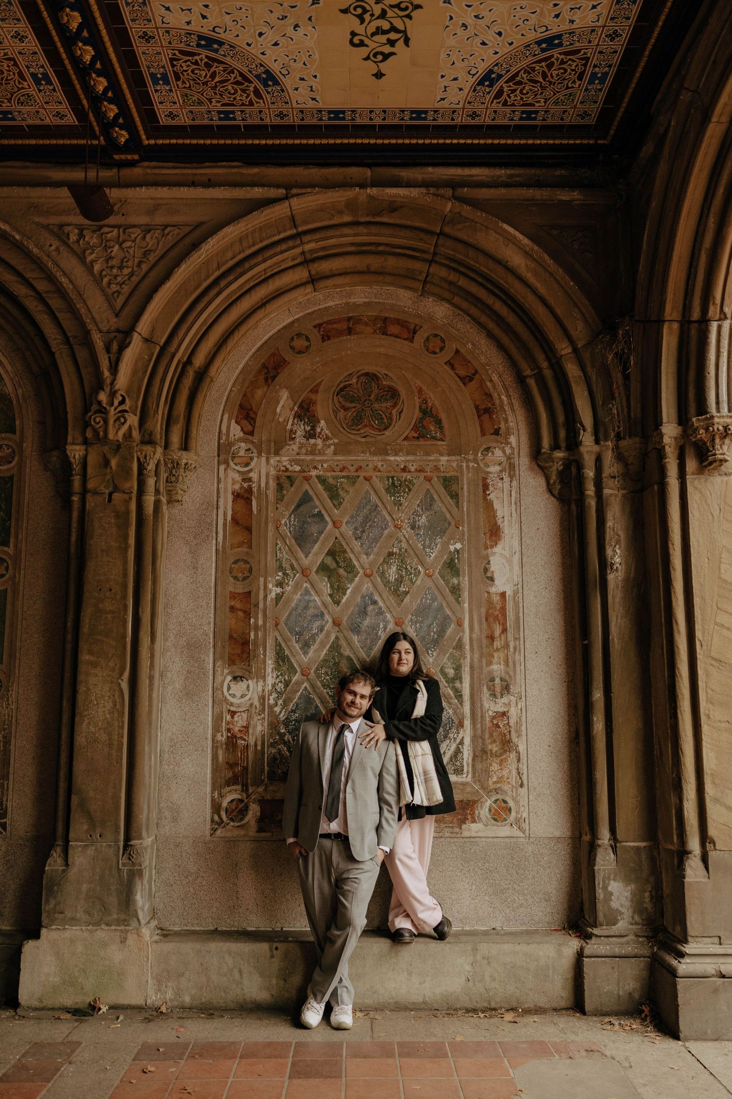 A couple poses in a series of romantic shots under ornate stone archways with vintage wall murals and decorative details.