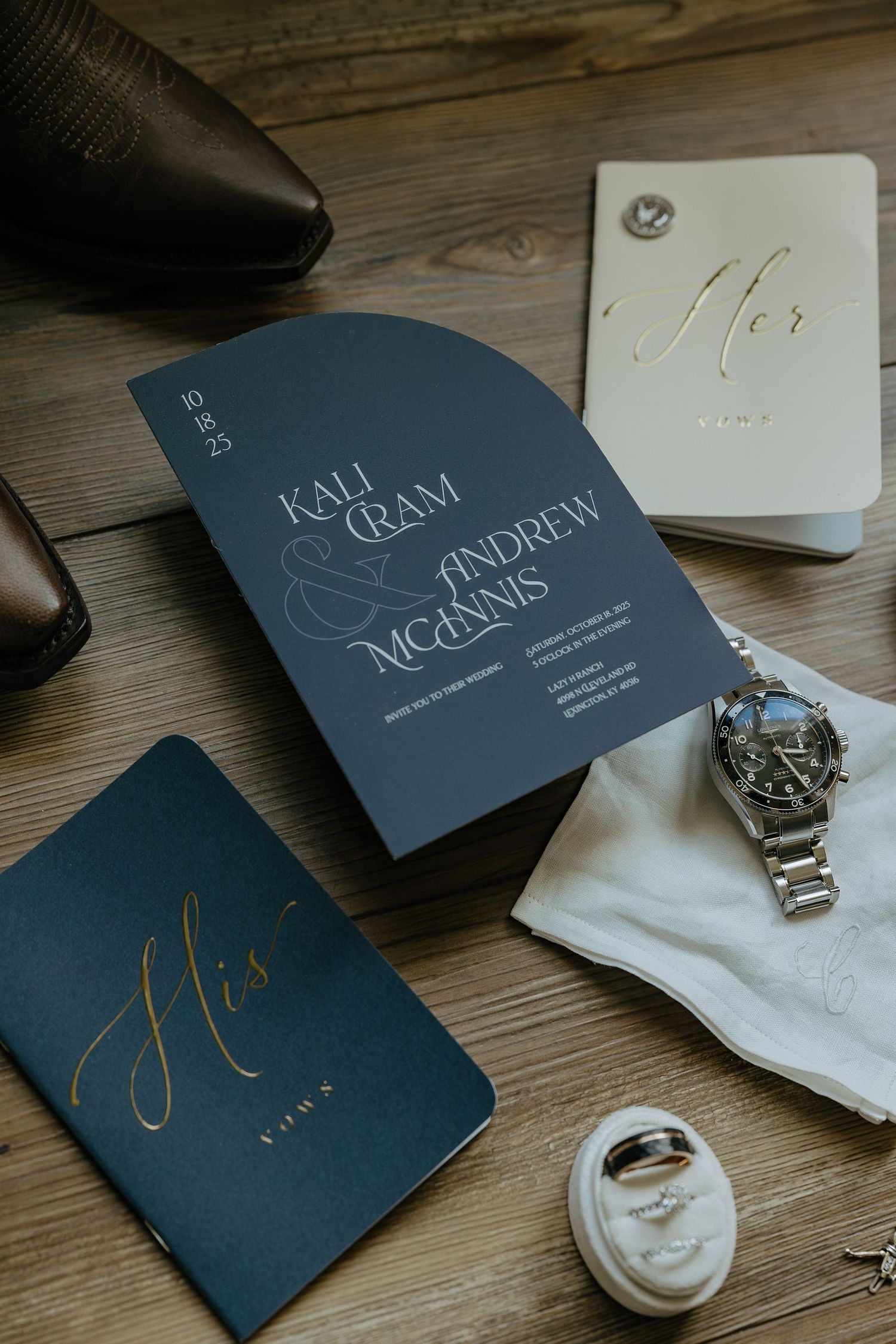 Elegant navy blue wedding stationery with gold calligraphy displayed on wooden surface with watch and accessories.