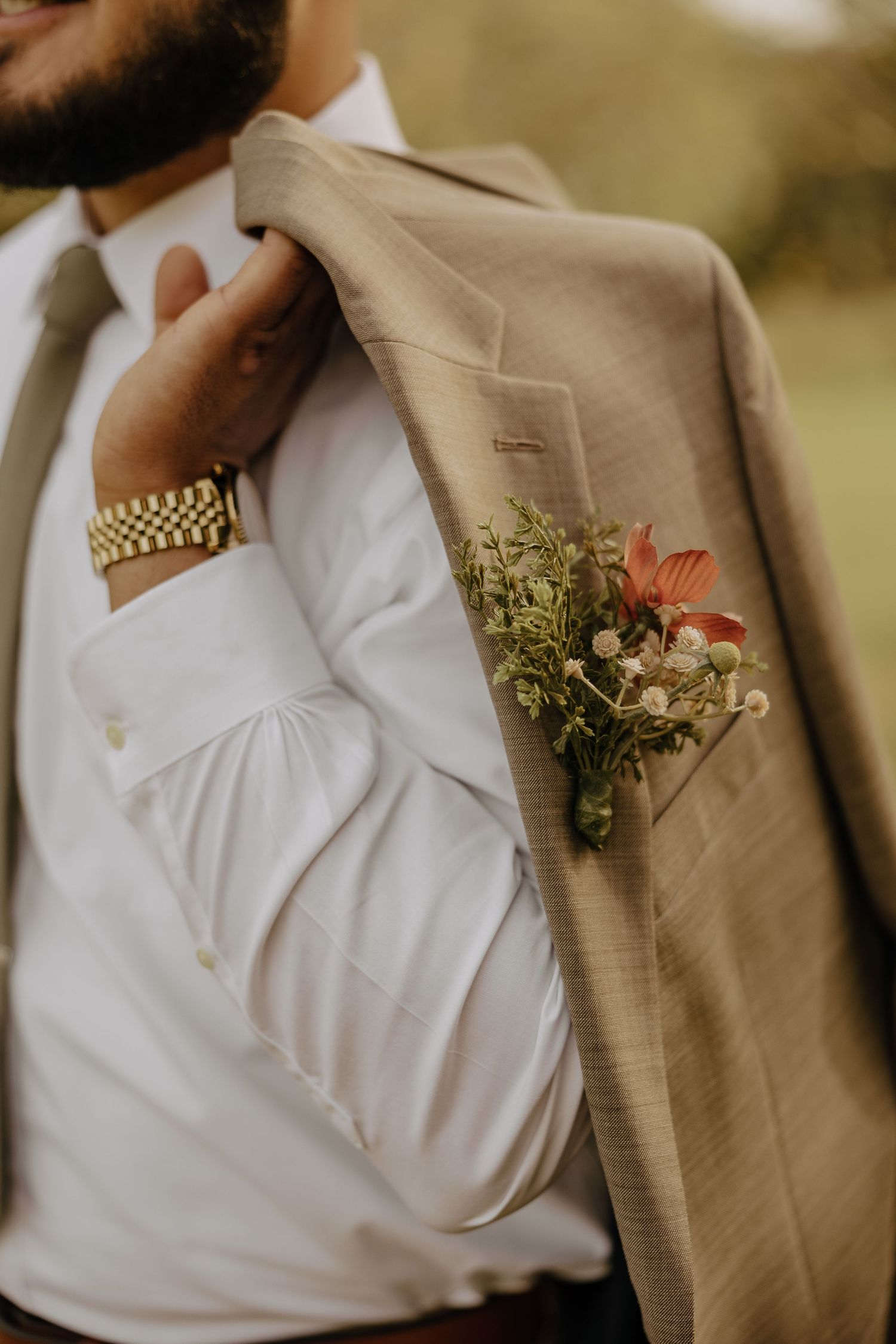 Beige suit jacket with floral boutonniere and white dress shirt details.