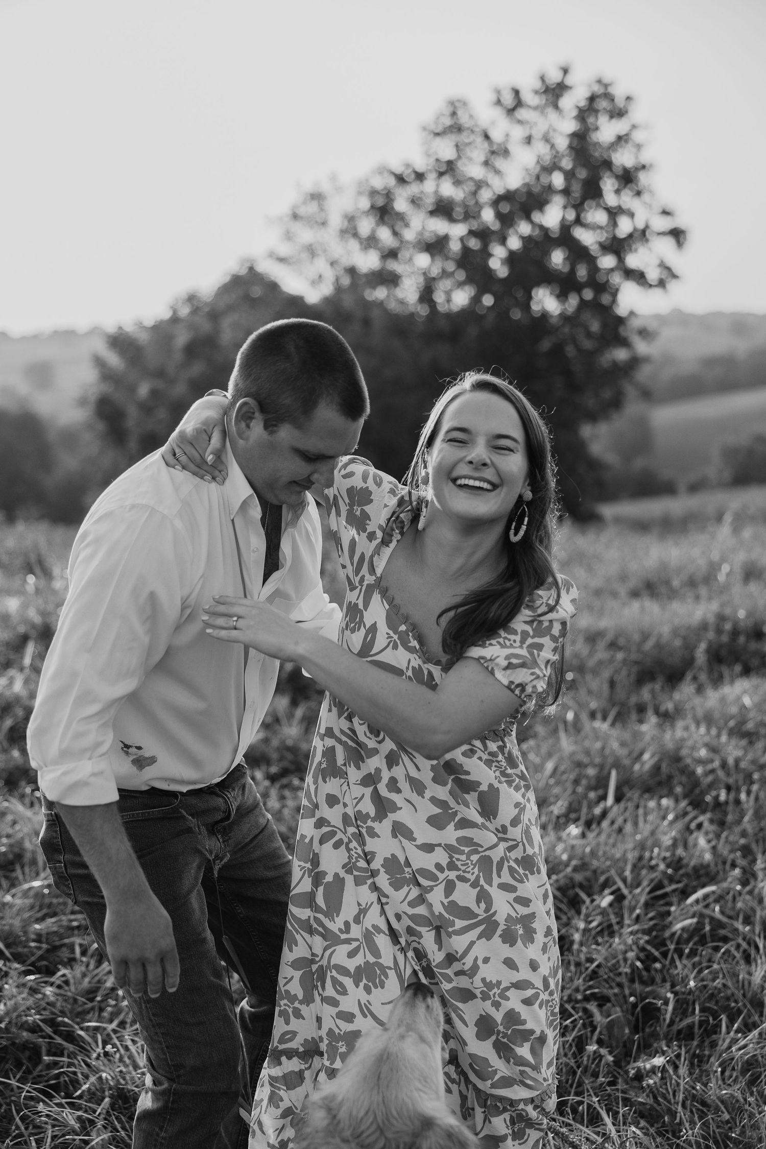 Black and white photo of a couple laughing together in a wildflower meadow.