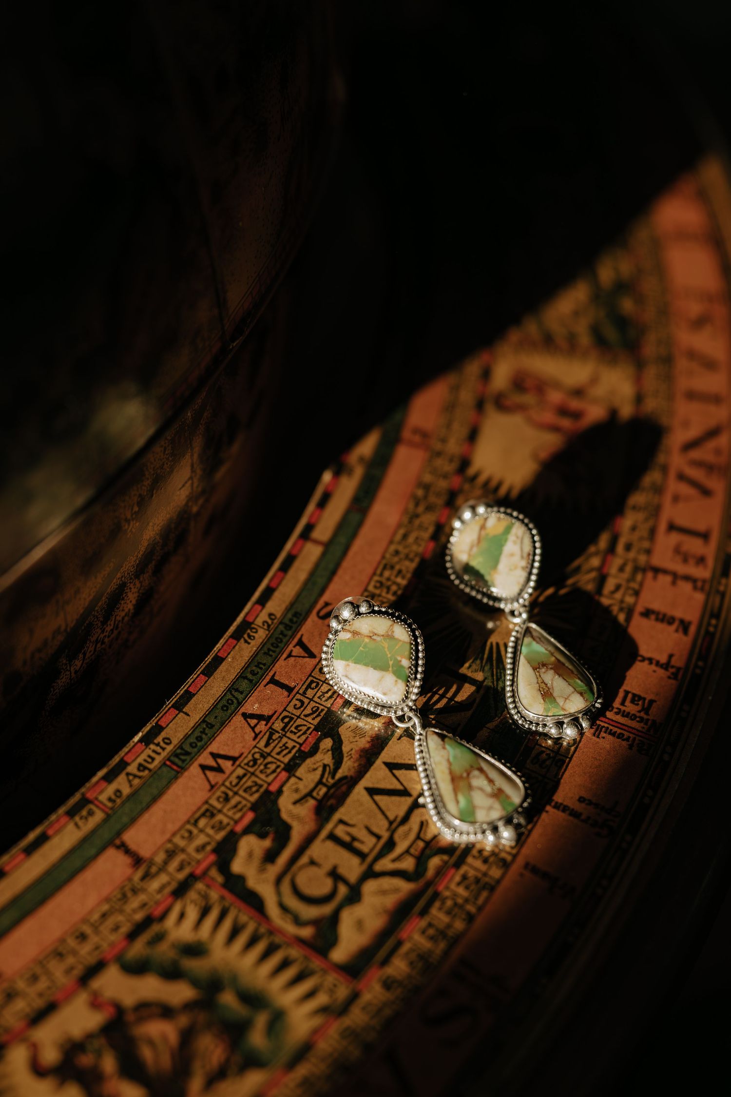 Vintage-style jewelry photographed on antique map with dramatic lighting.