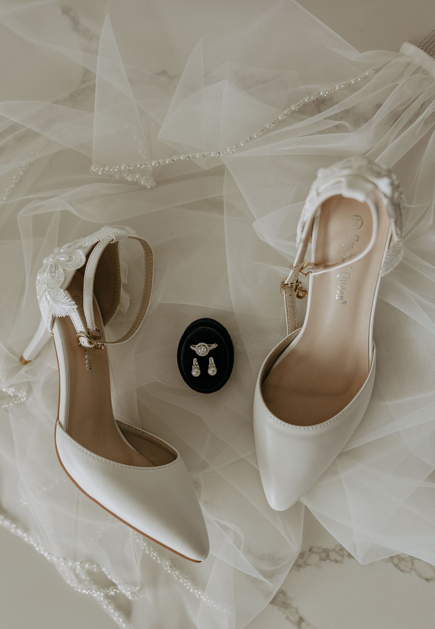 Elegant white satin bridal shoes with delicate straps displayed against soft tulle fabric.