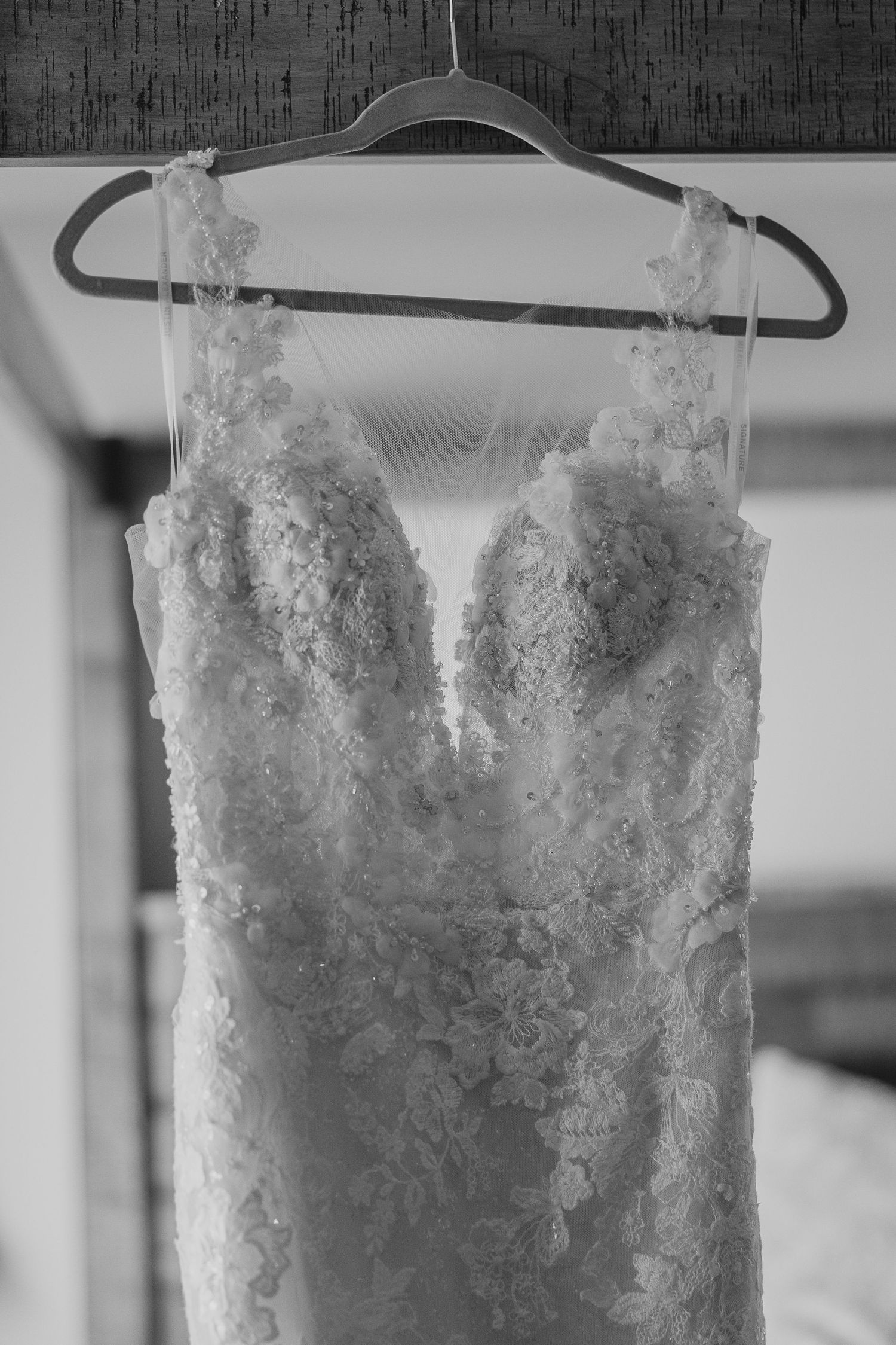 A delicate lace wedding dress hanging on display, shown in black and white.