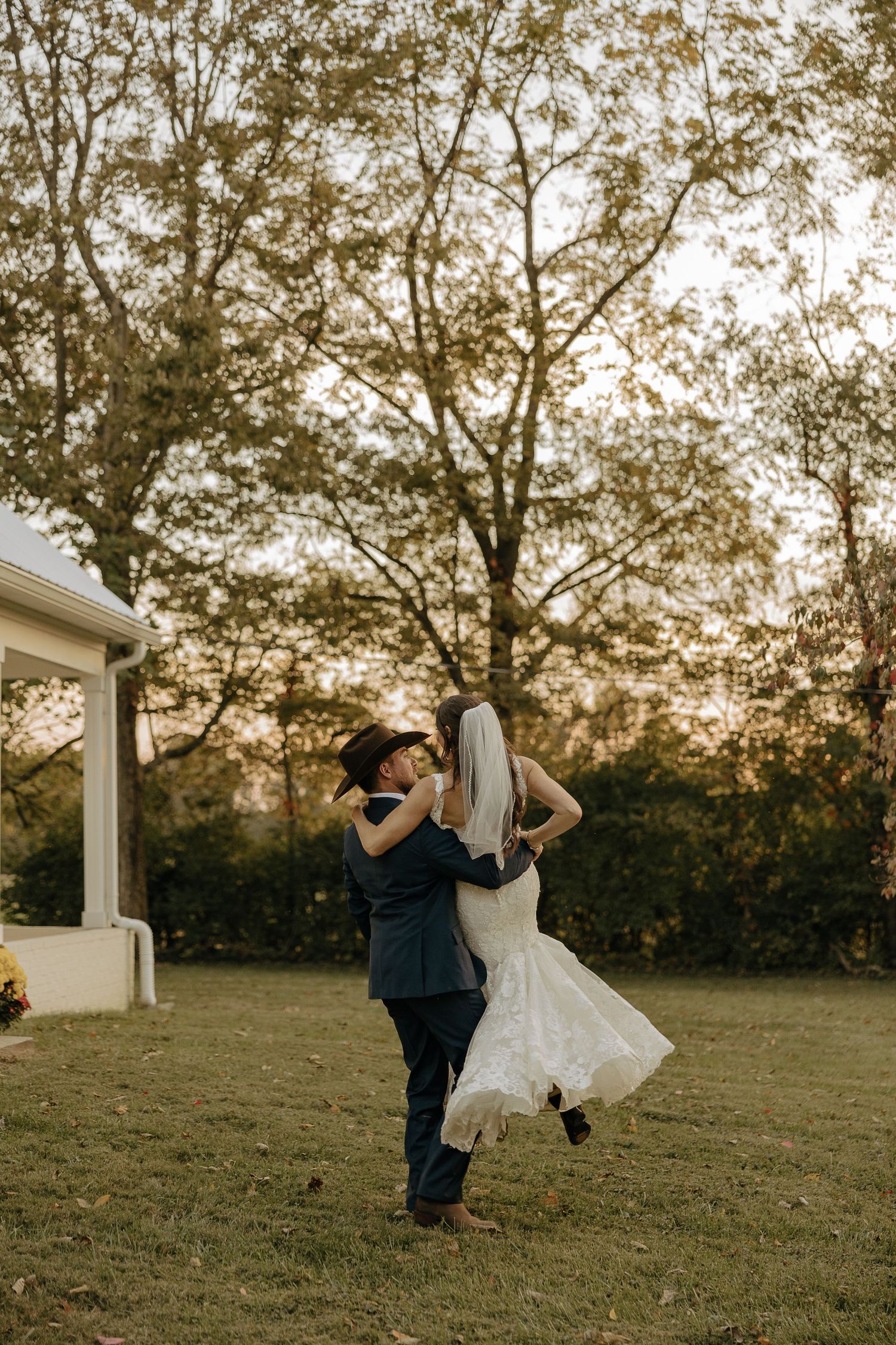 A playful wedding couple dances on a grassy hill during golden hour.