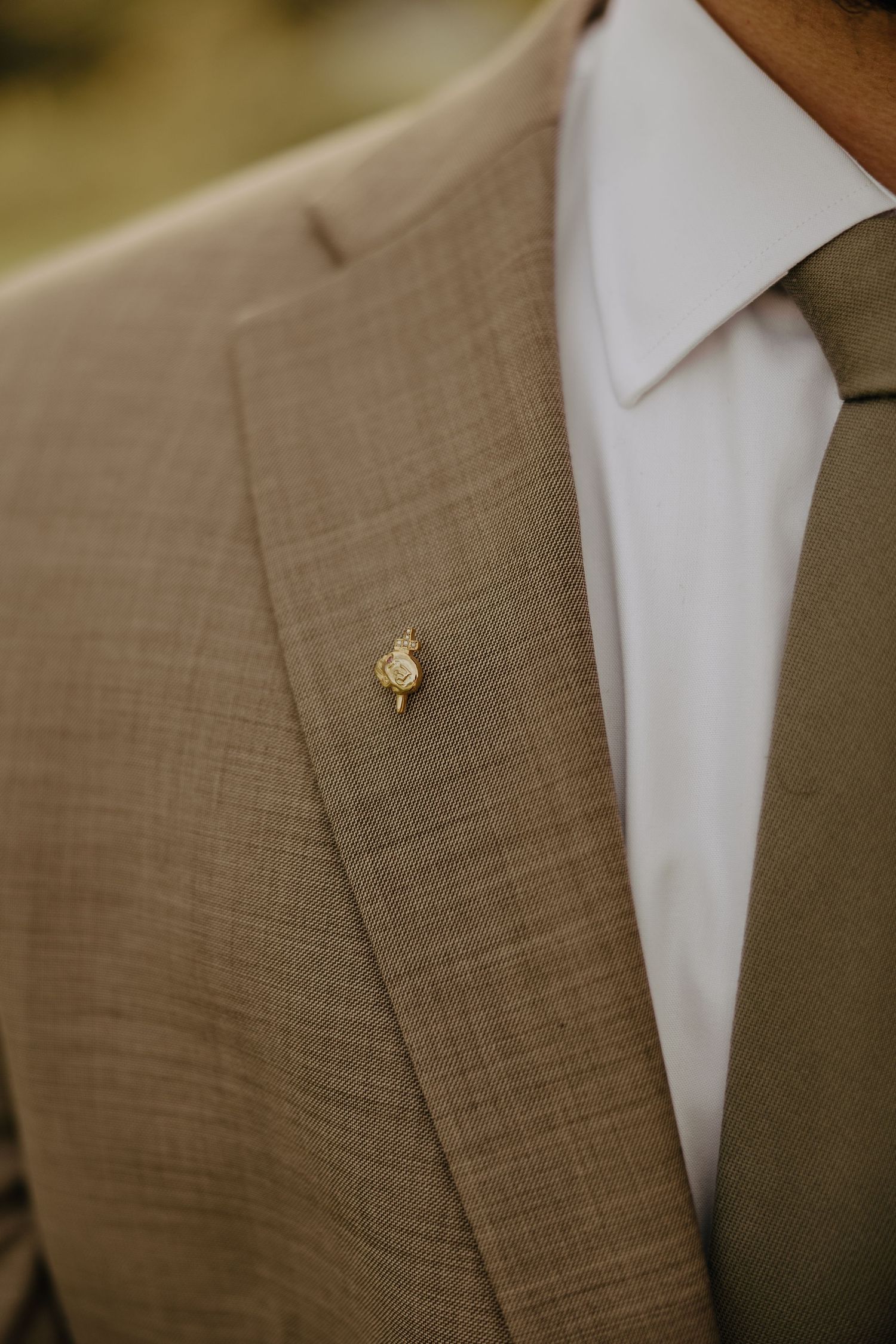 Close-up detail of a gold butterfly pin on a tan suit lapel.