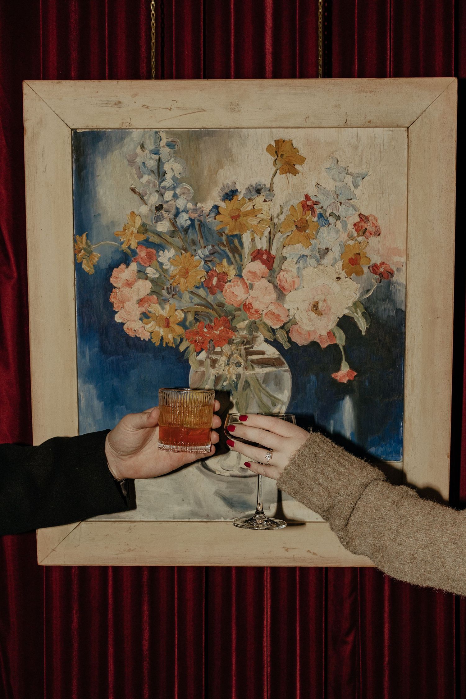 Still life painting of flowers in vases displayed against deep red curtains.