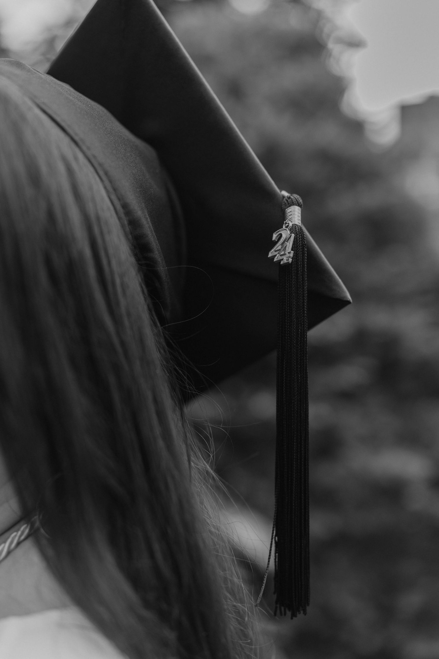 Black and white close-up detail of graduation cap tassel against blurred background.