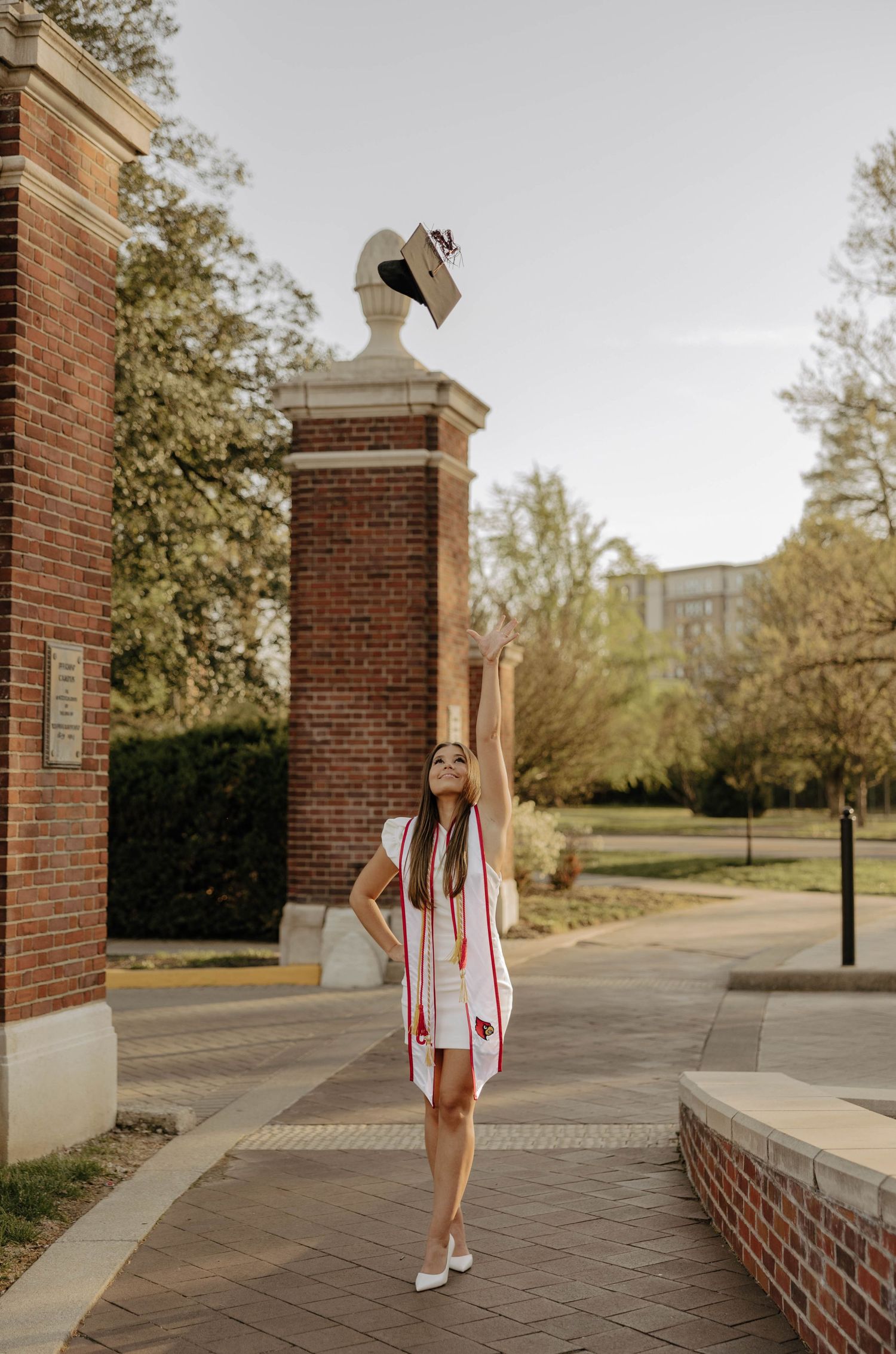 Graduation portraits showing graduate walking near brick building with red stoles.