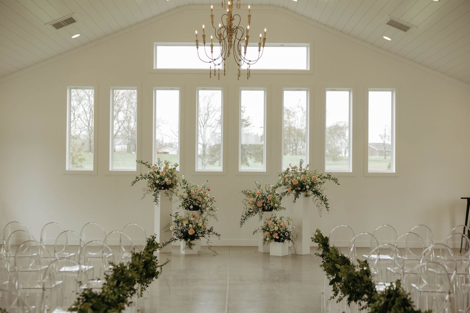 Elegant white wedding venue interior with rows of chairs and crystal chandeliers.
