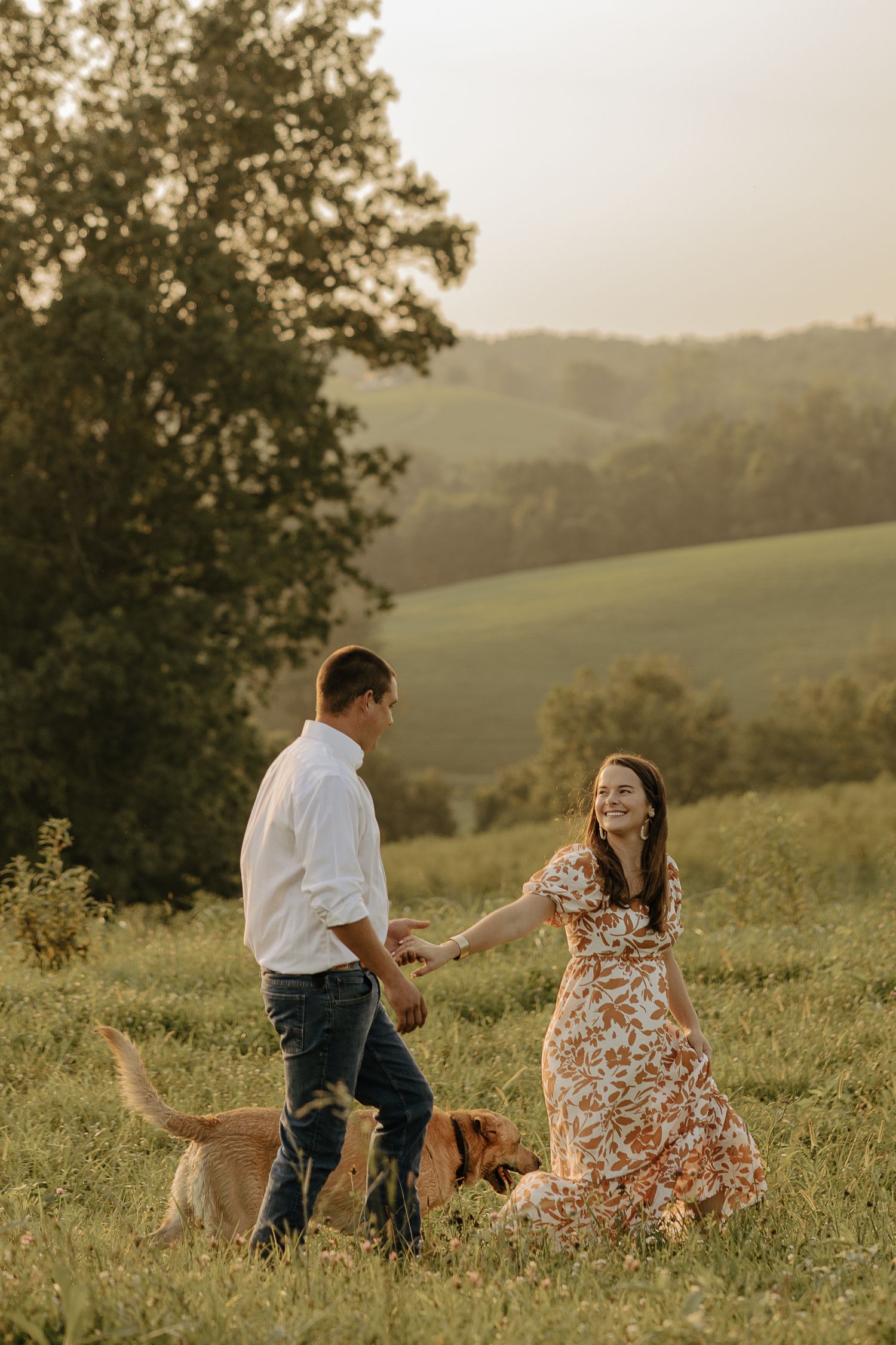 A couple sits in a wildflower meadow during sunset while sharing a playful moment together.
