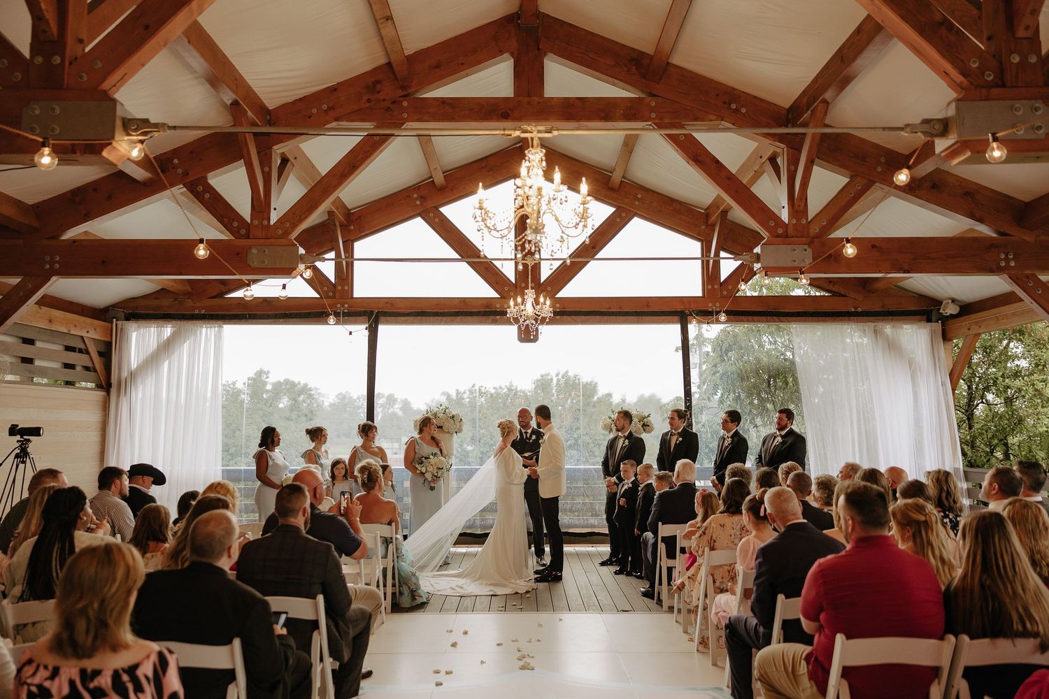Wedding ceremony venue with exposed wooden beams and white draping in a rustic indoor setting.
