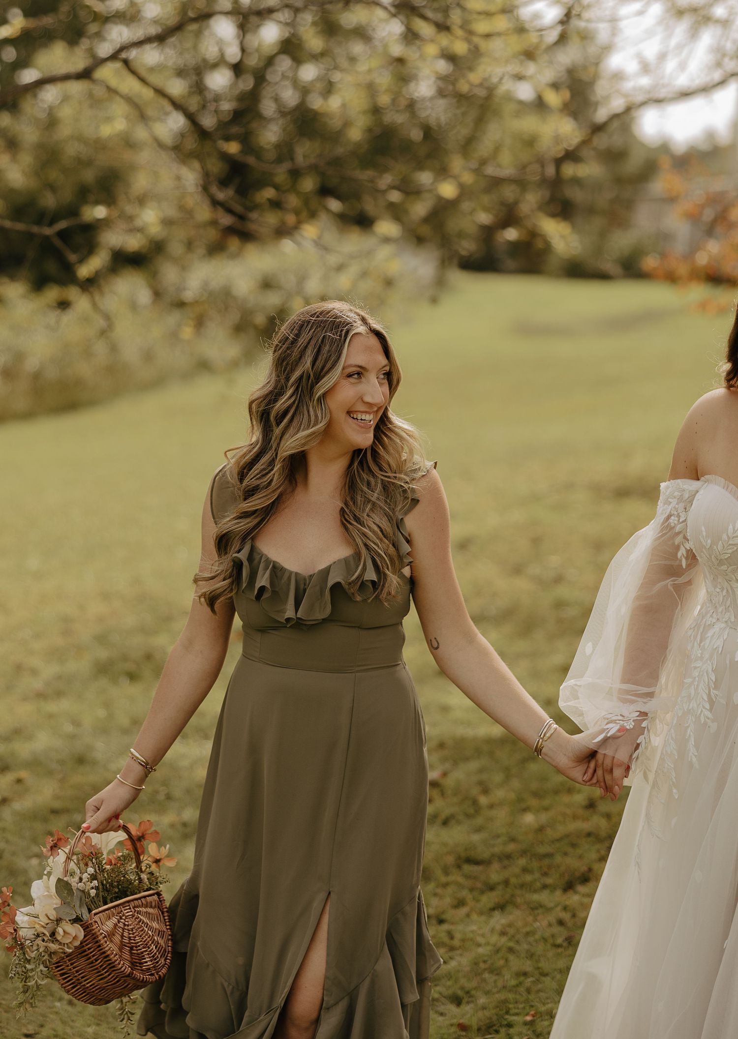 Bridesmaids in olive green dresses walking together outdoors during an autumn wedding celebration.