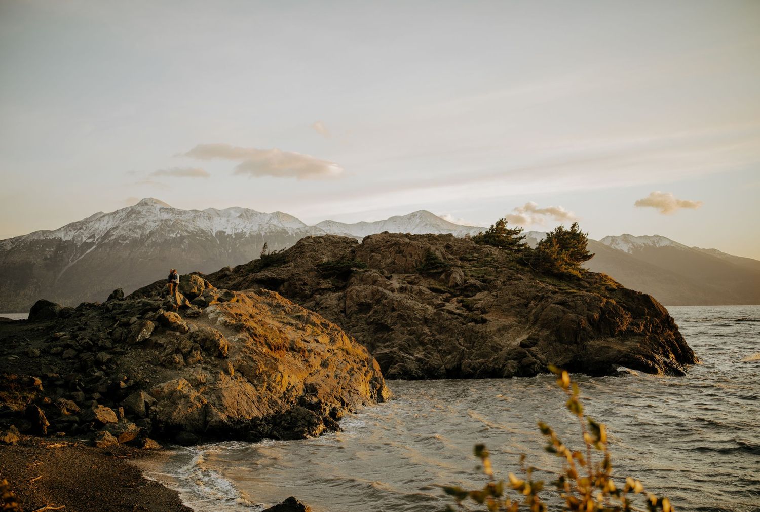 A panoramic sequence of snow-capped mountains and rocky coastline at sunset along a rugged shoreline.