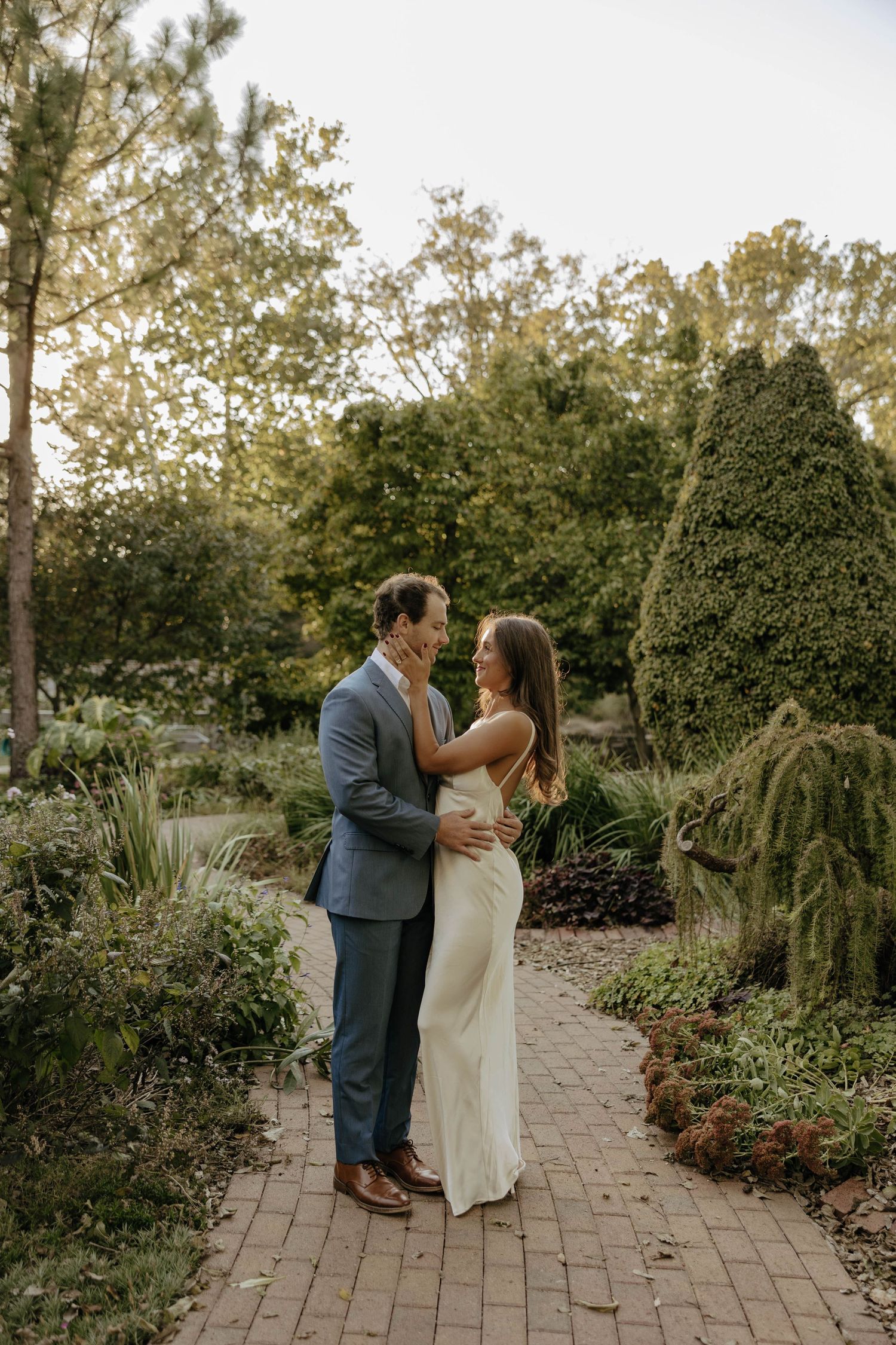 Couple walking and dancing together on a brick path surrounded by lush garden landscaping.