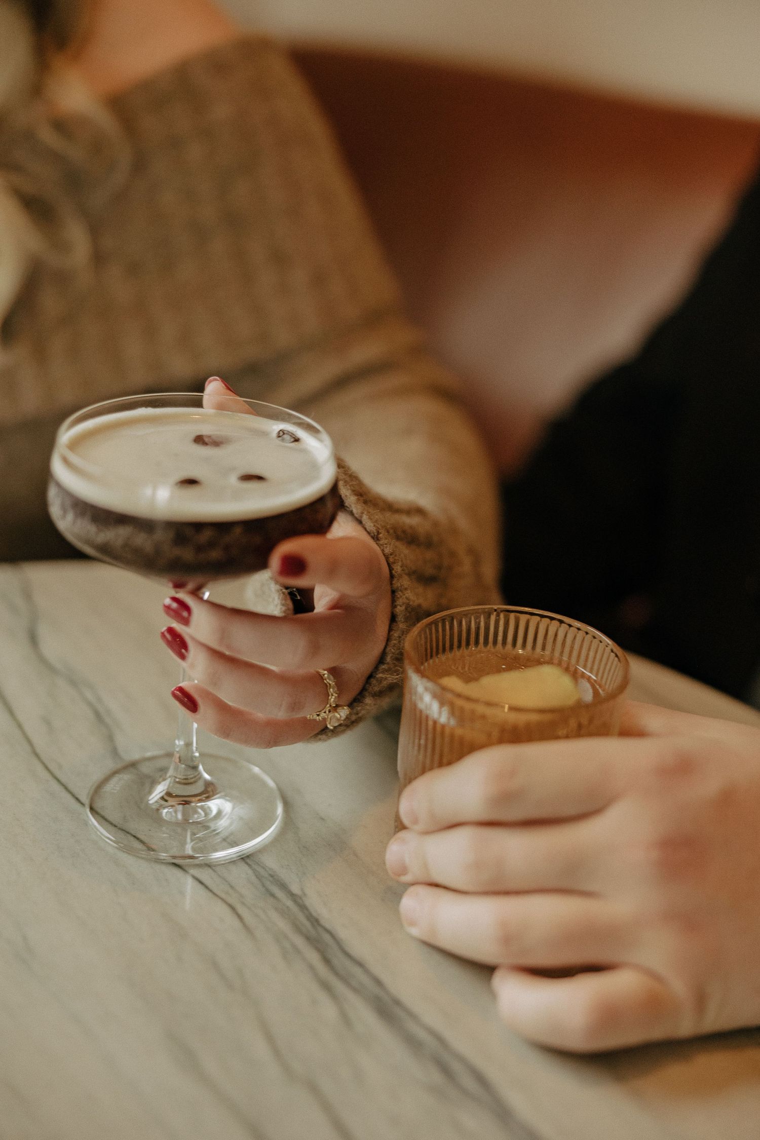 Close-up shot of hands holding elegant cocktail glasses with pink drinks.