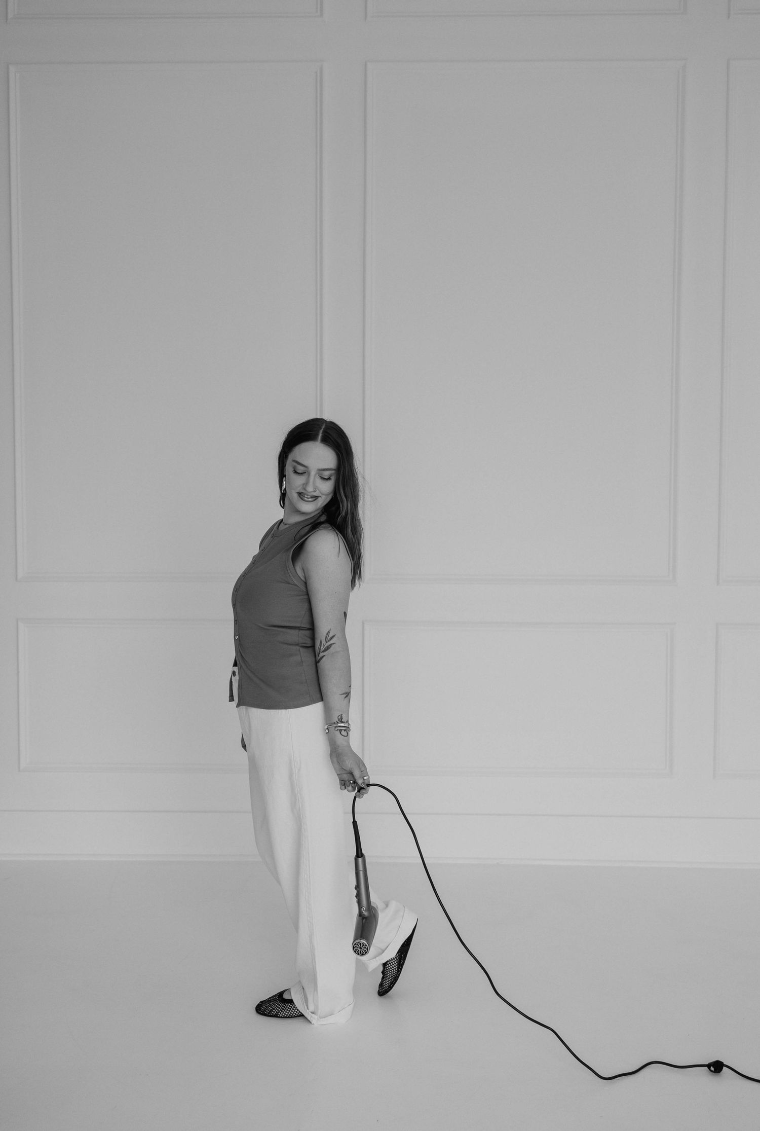Black and white photo of person posing with styling tool against paneled wall.