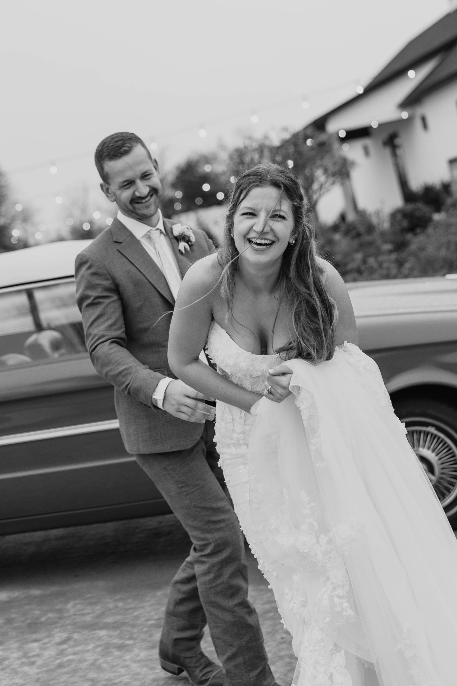 Black and white photos capture playful moments between couple by classic car.