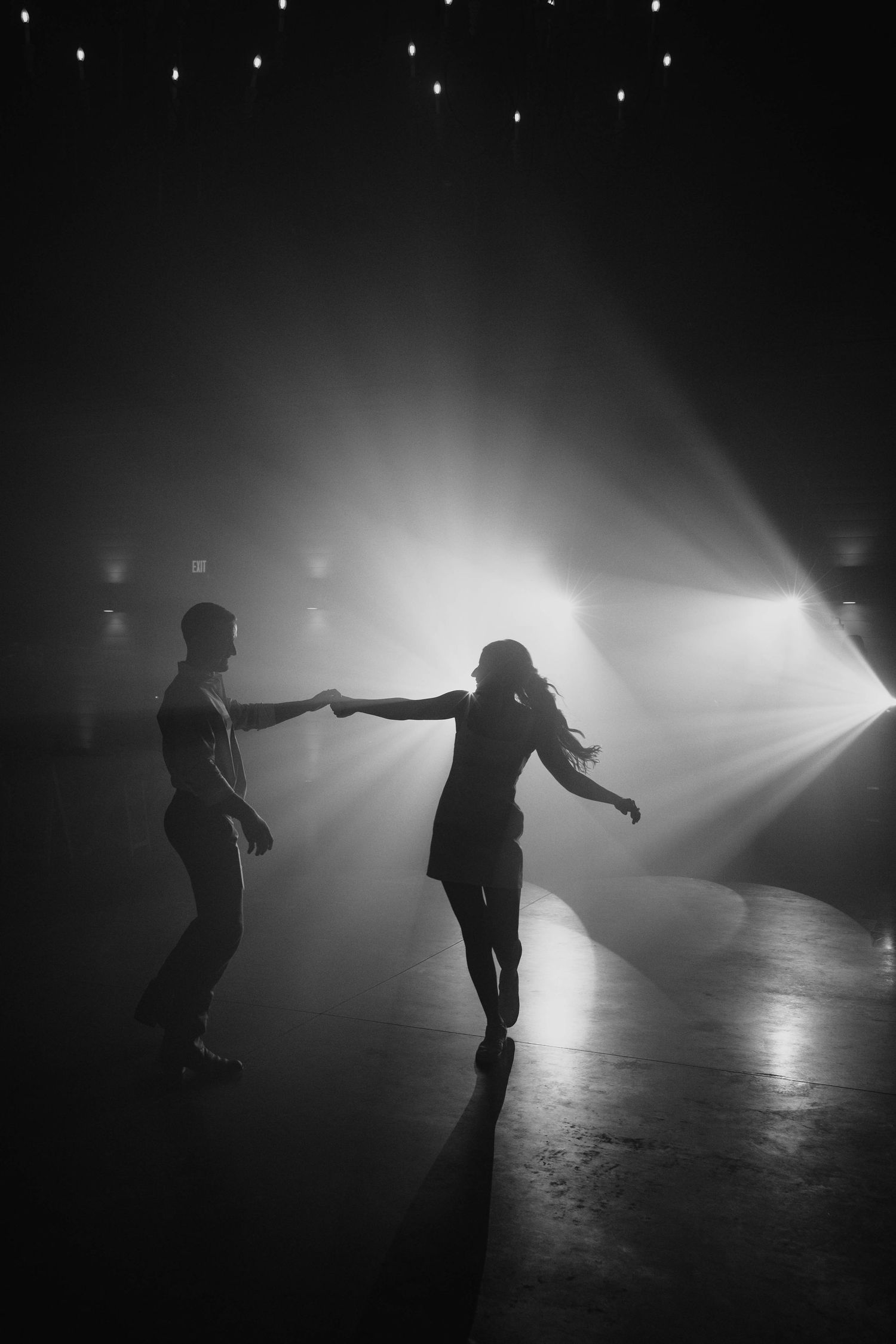 Two silhouettes dance together in dramatic backlighting with beams of light creating a misty, atmospheric scene.