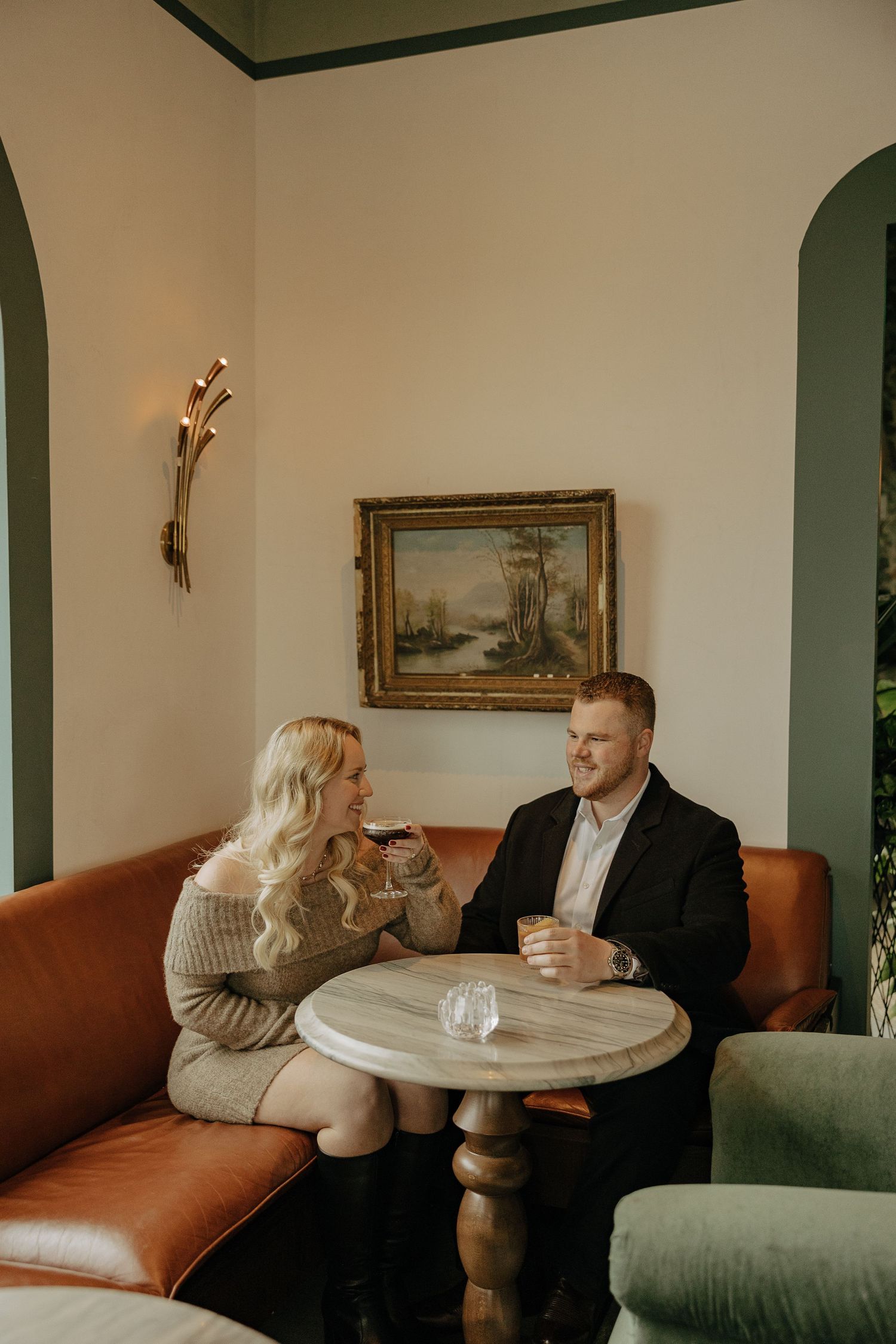 Couple sharing intimate conversation at a cozy restaurant table with leather seating and arched windows.