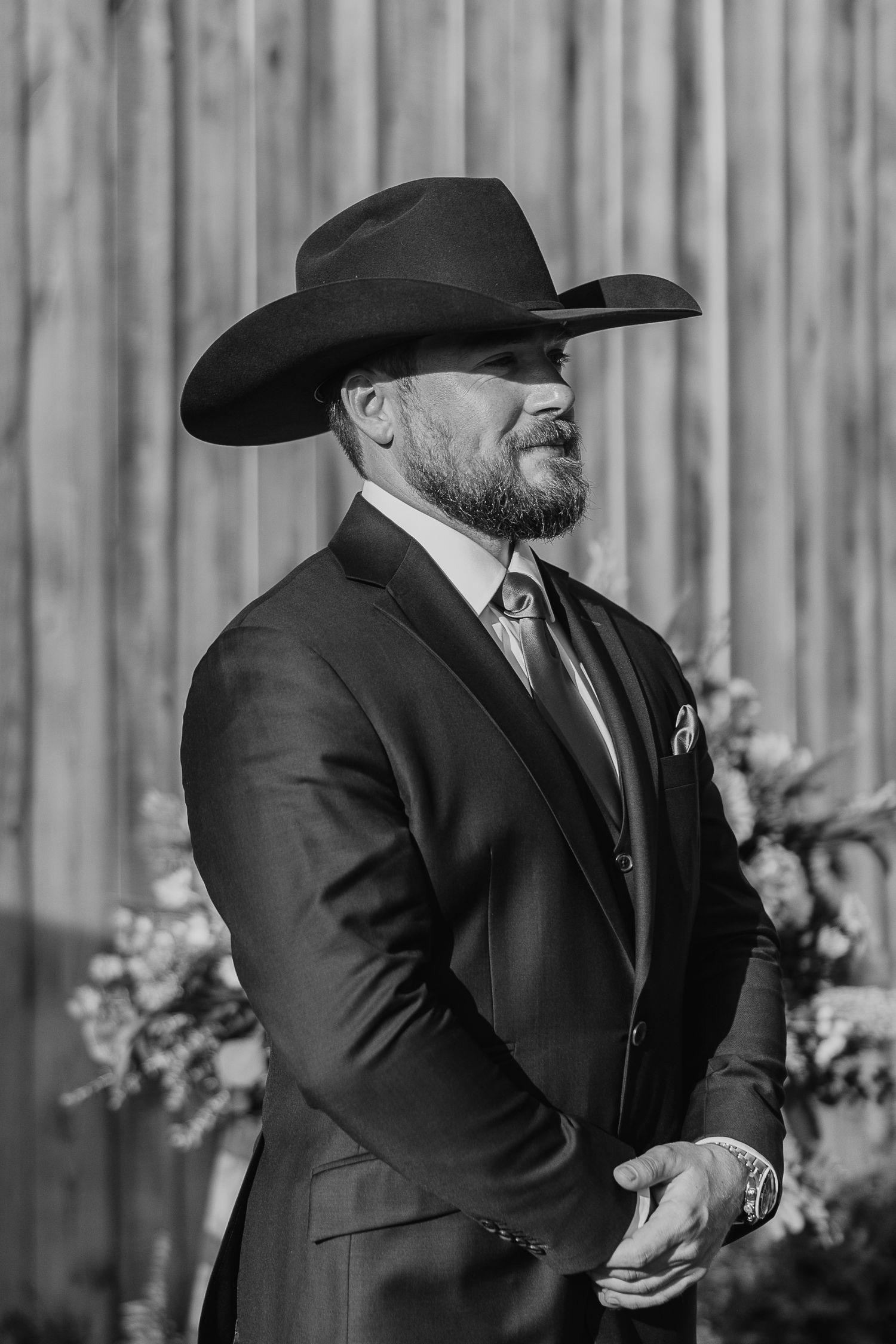 Wedding party members in dark suits and cowboy hats share a candid moment.