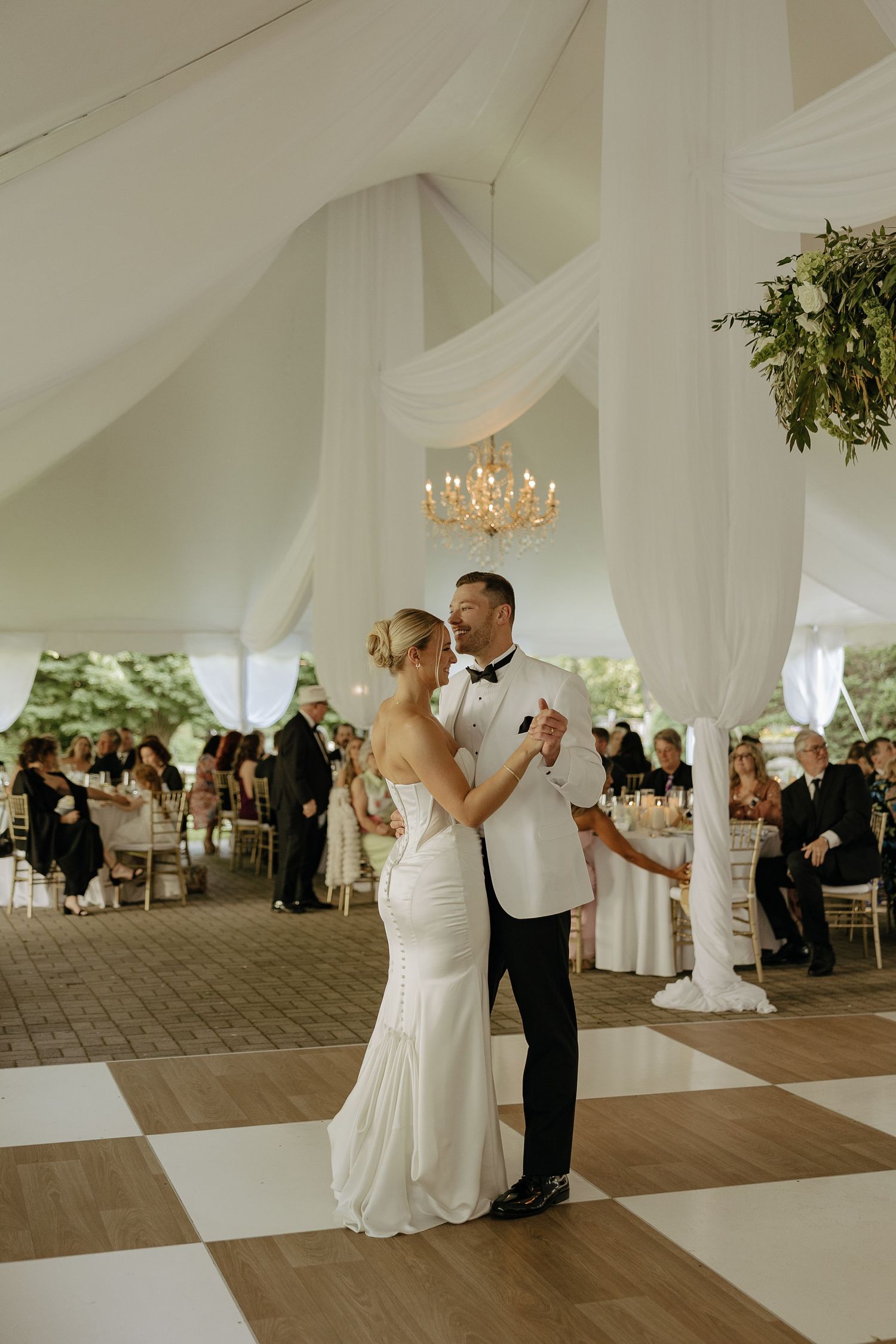 Bride and groom share first dance under draped tent with chandelier at reception.