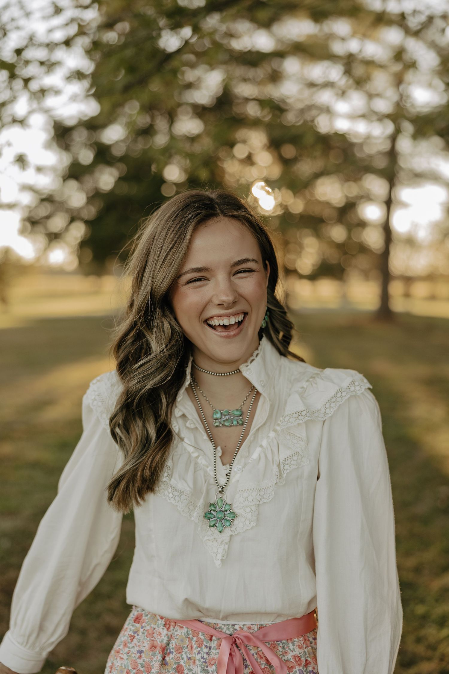 Person wearing white blouse and turquoise necklace in natural outdoor lighting.
