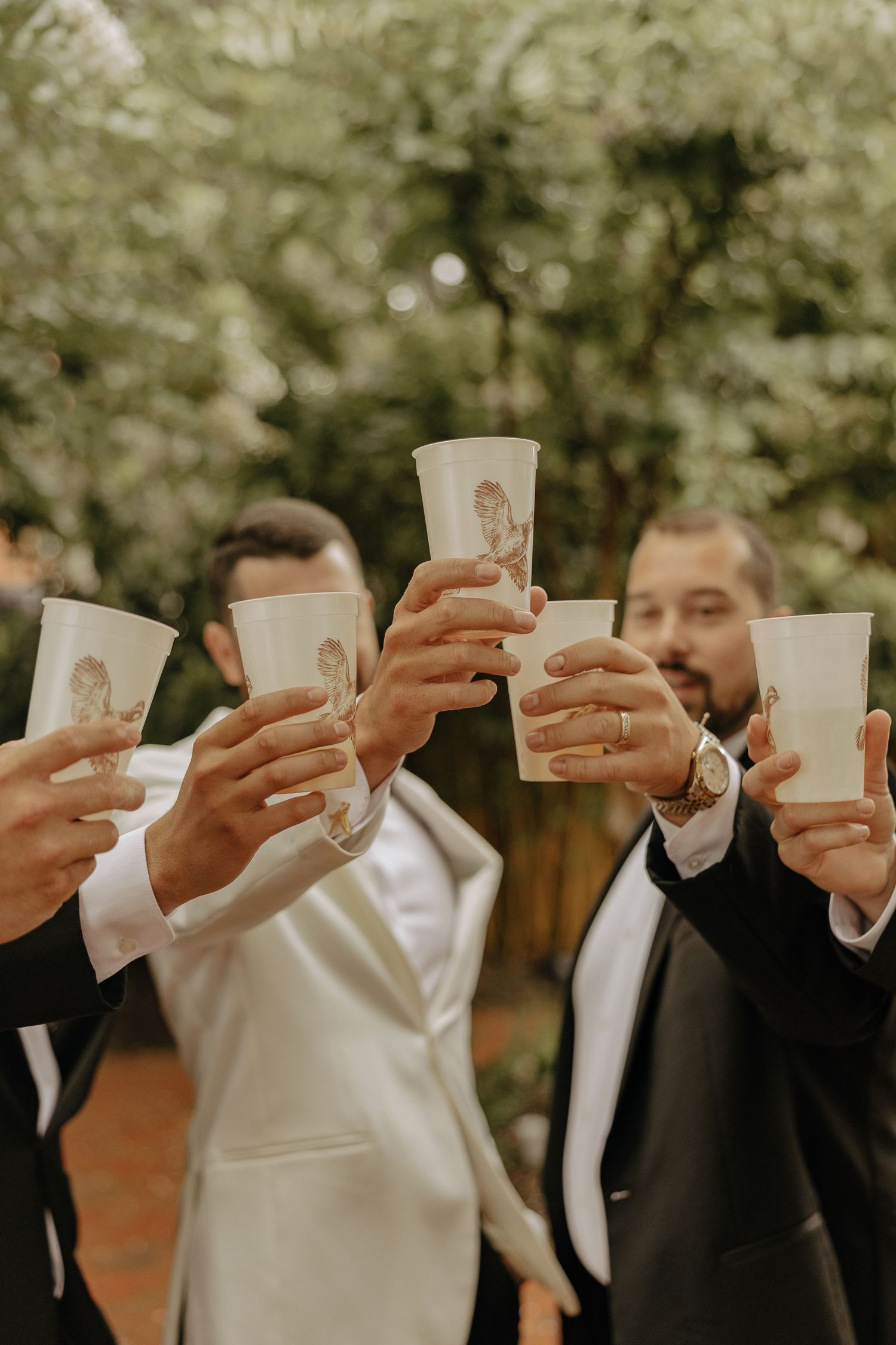 Wedding party in formal attire raising glasses for a celebratory toast outdoors.