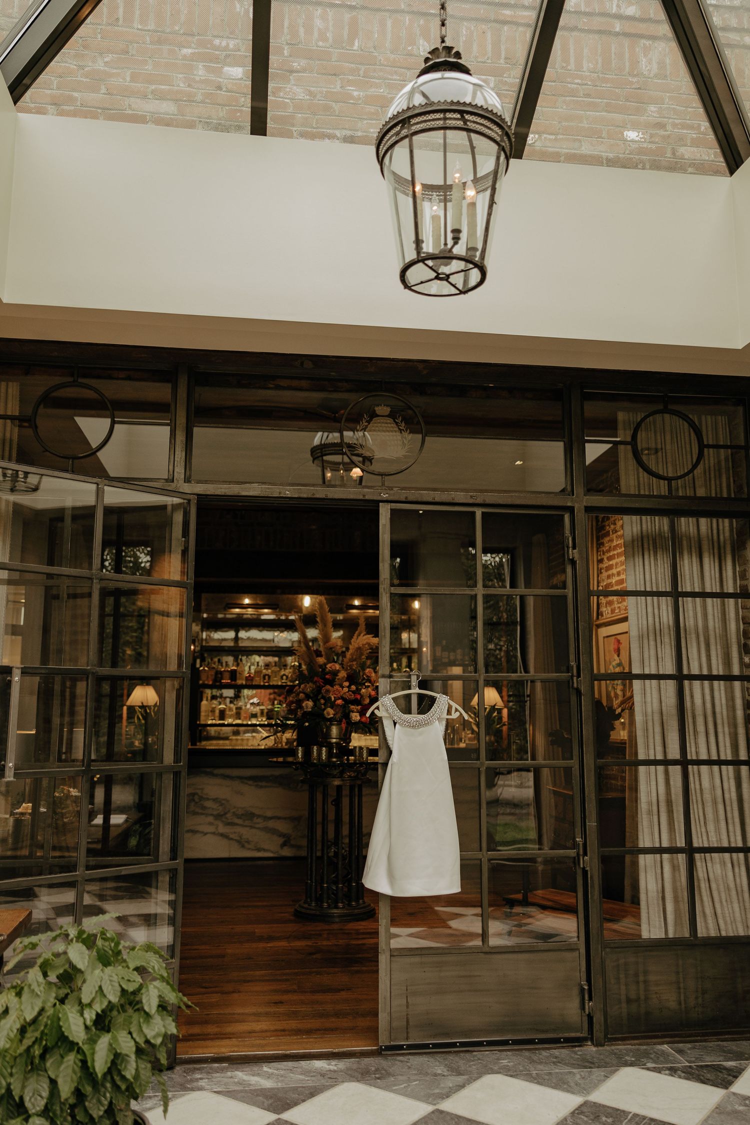 White wedding dress hanging in storefront window beneath elegant vintage lantern.