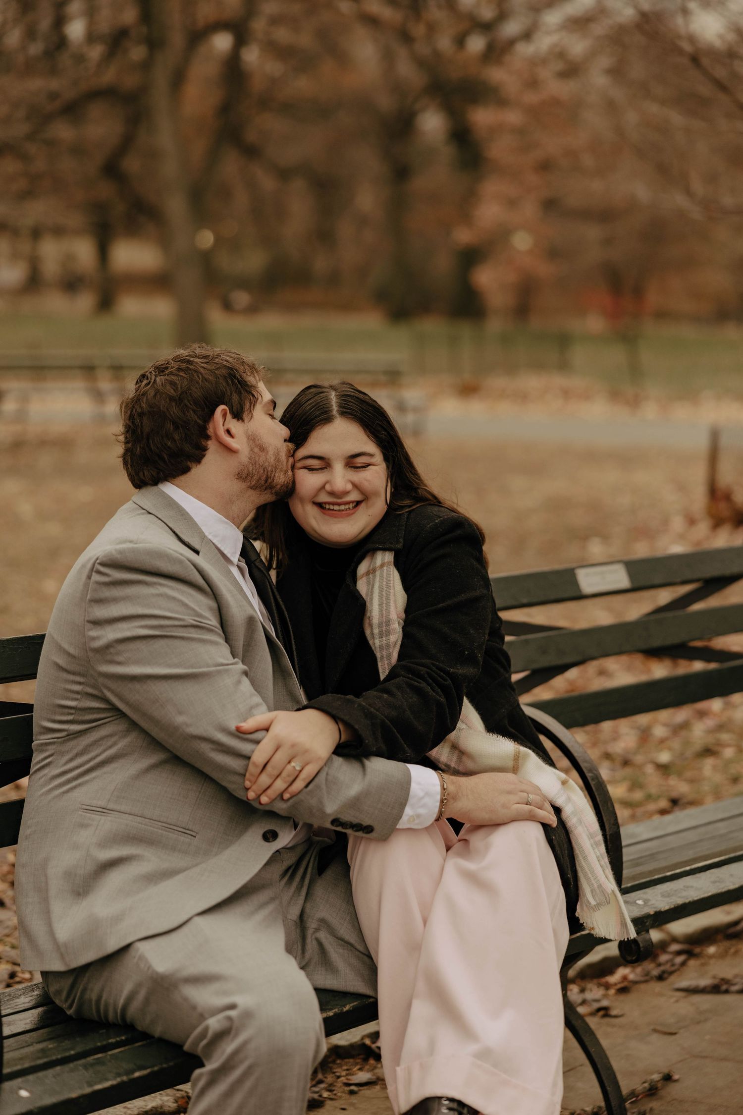 A romantic couple shares tender moments while sitting on a park bench during autumn.