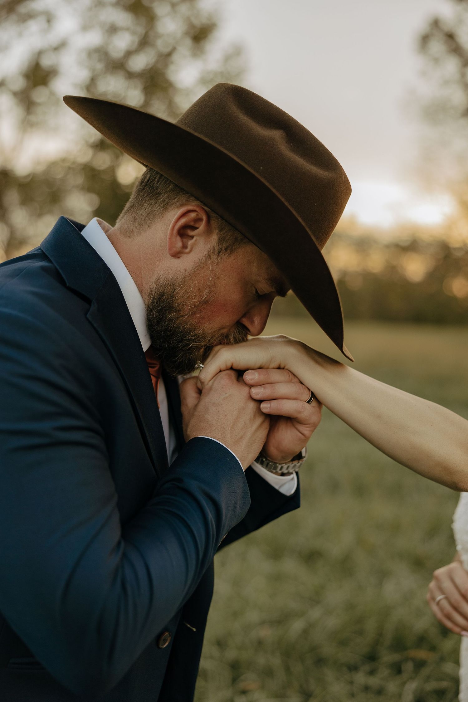 Emotional wedding moment captured during sunset with cowboy hat and formal attire.