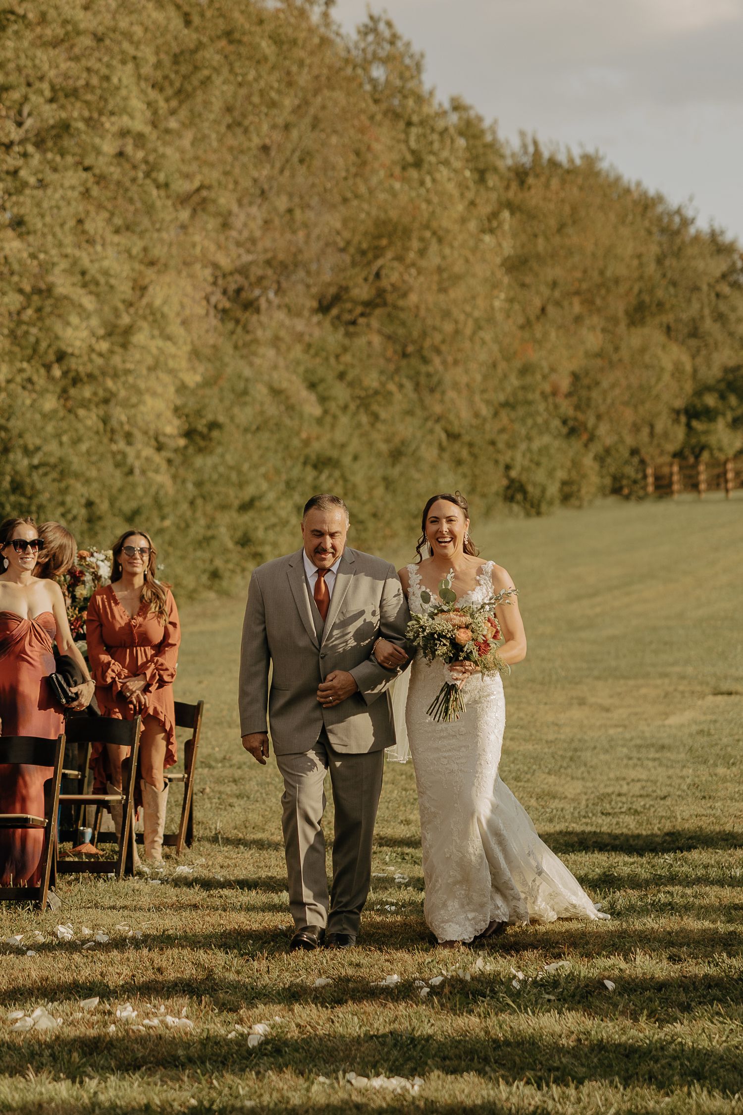 Wedding party walking across a sunlit grassy hill during golden hour.