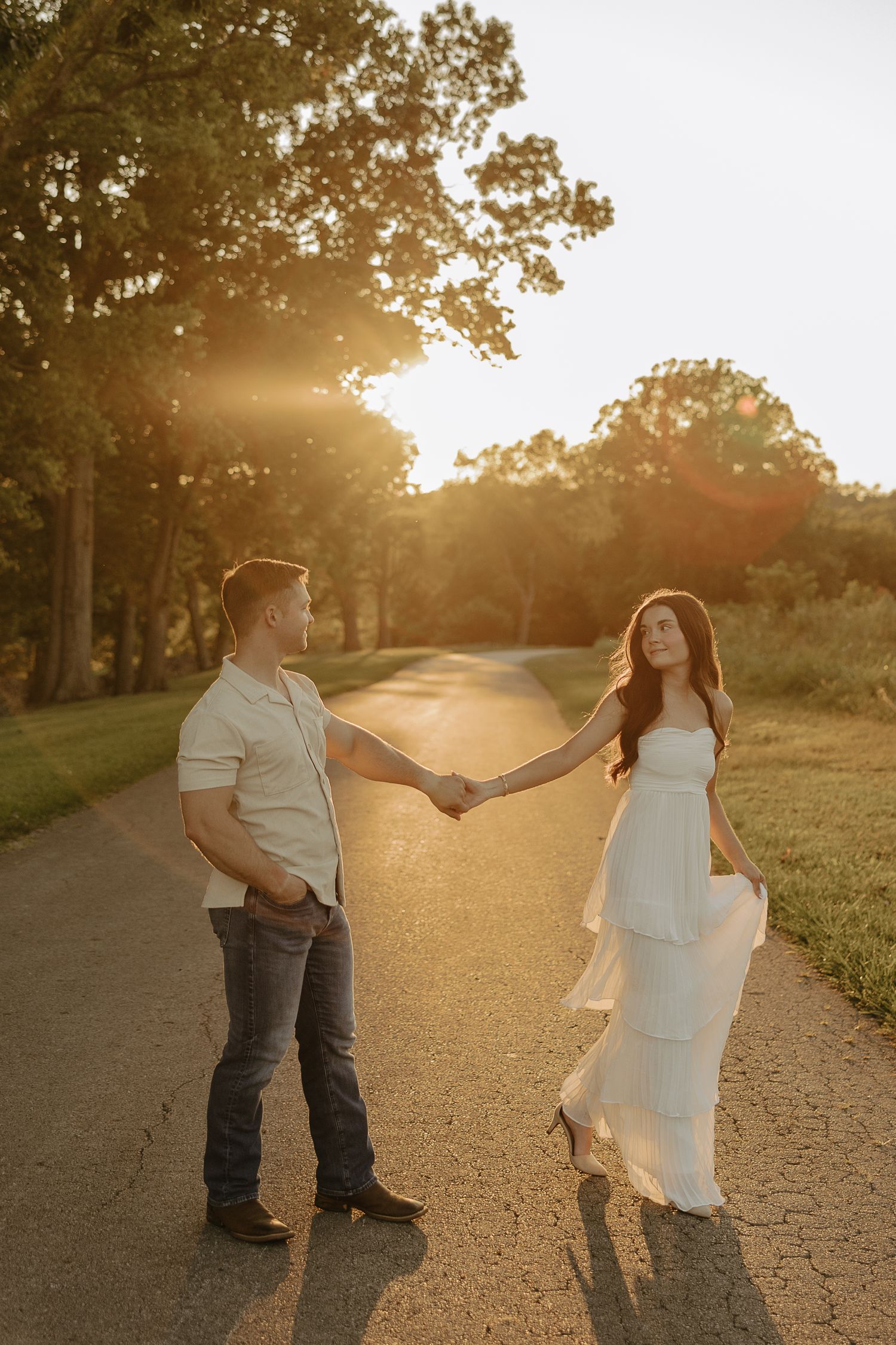 A couple dances playfully together on a sunlit dirt path during golden hour.