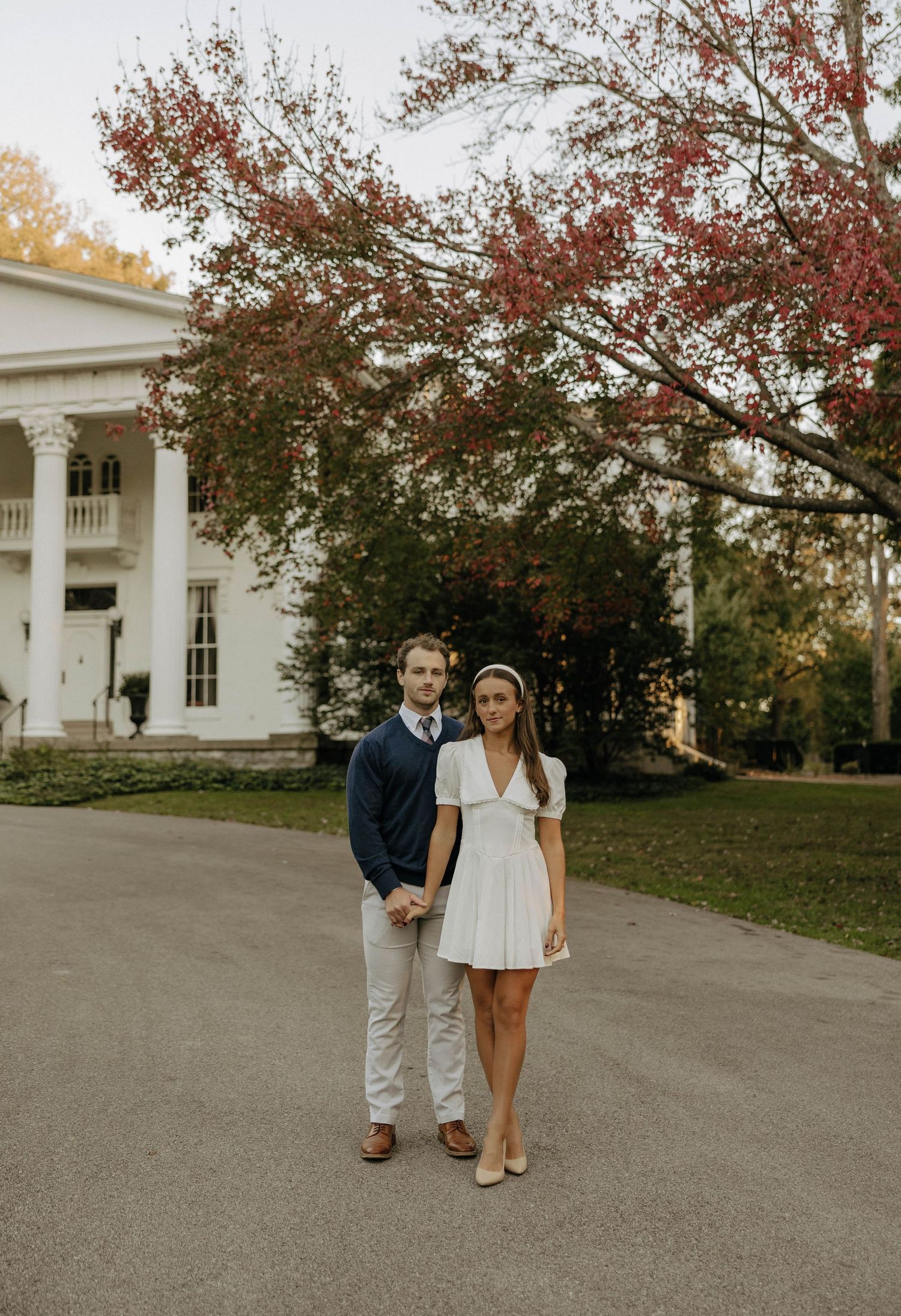 Couple walking together outside a grand white colonial-style building during autumn.