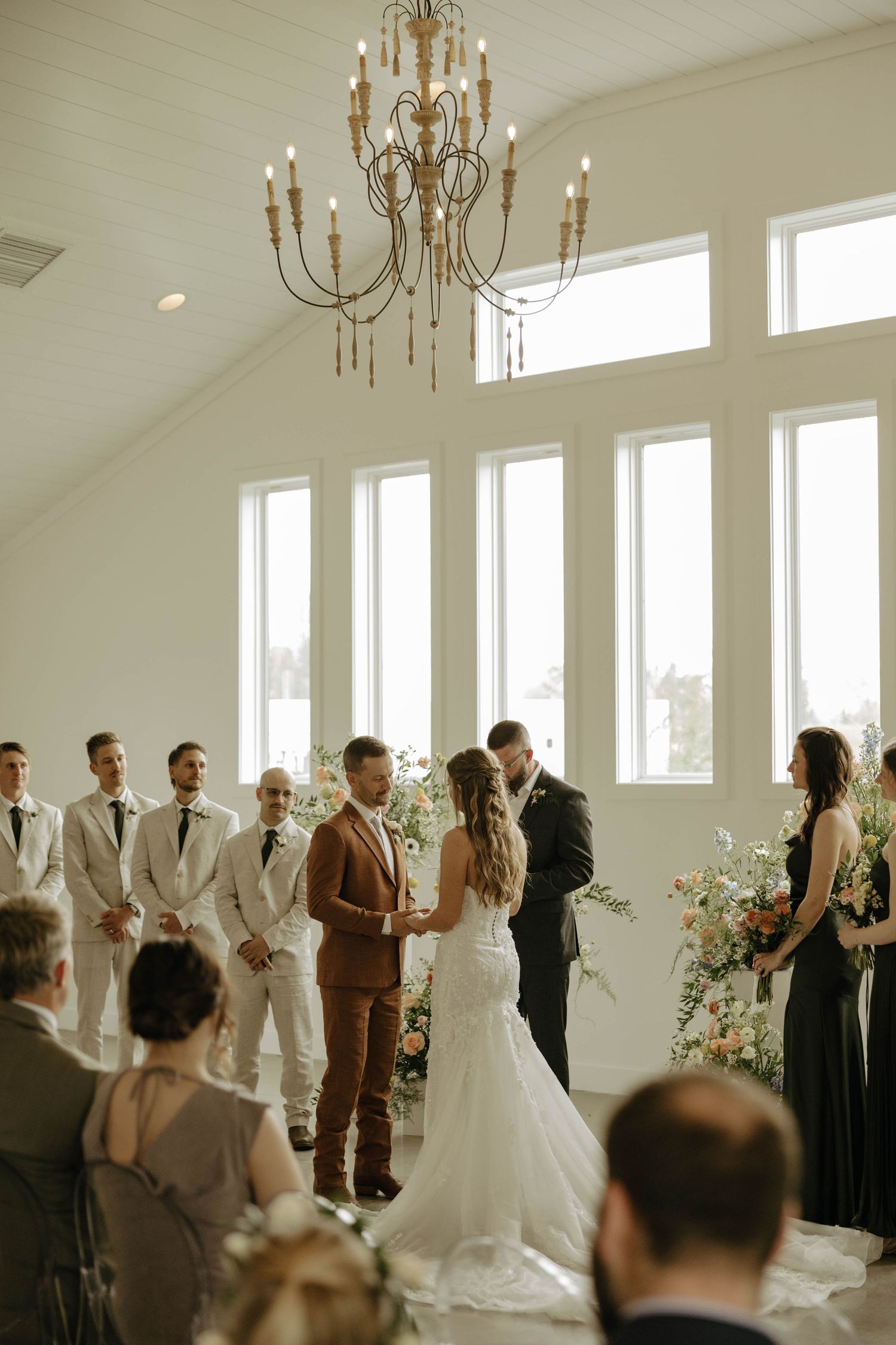 A wedding ceremony in a bright white room with large windows and an elegant chandelier.