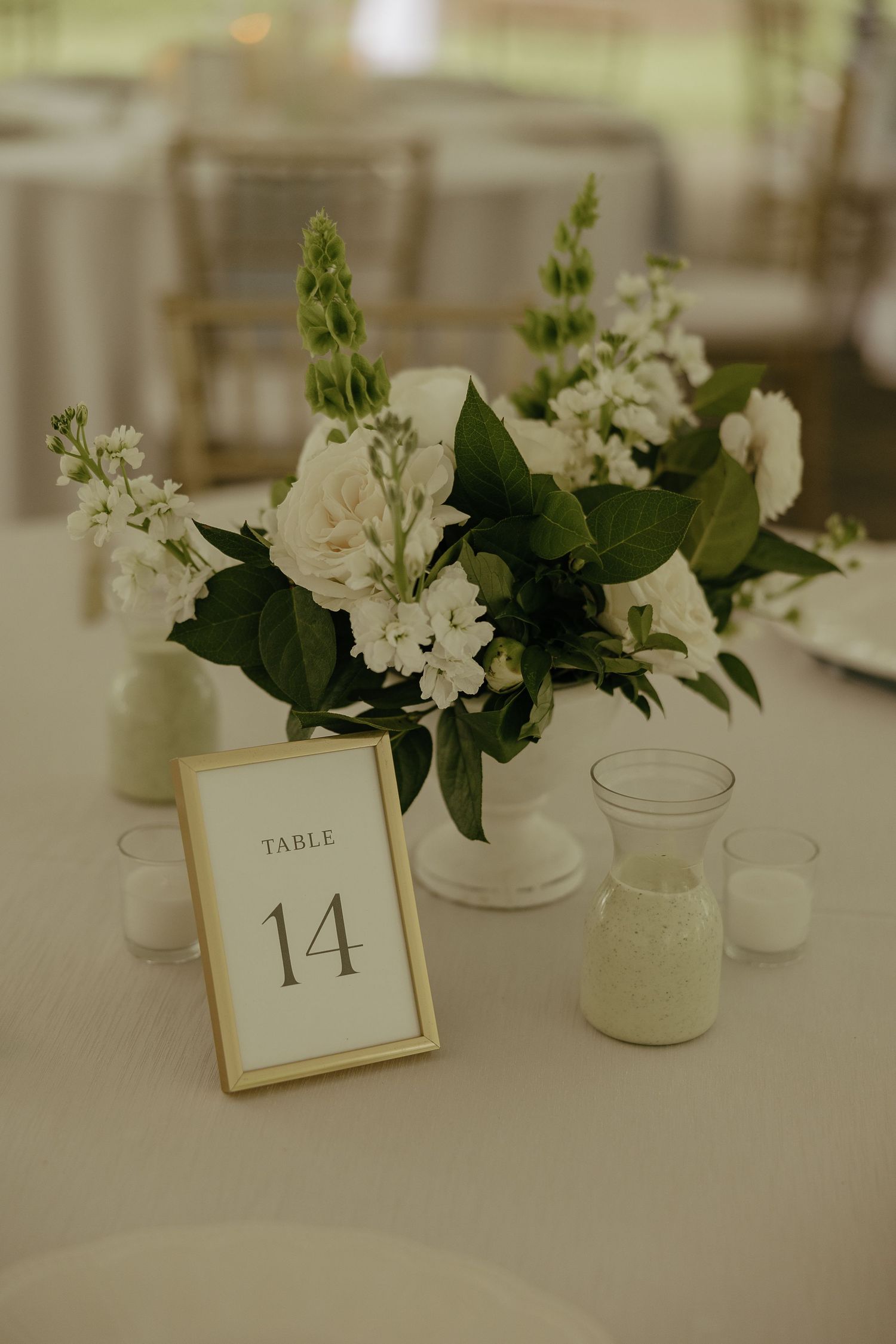 Elegant wedding Table 14 centerpiece with white roses and greenery in gold frame.