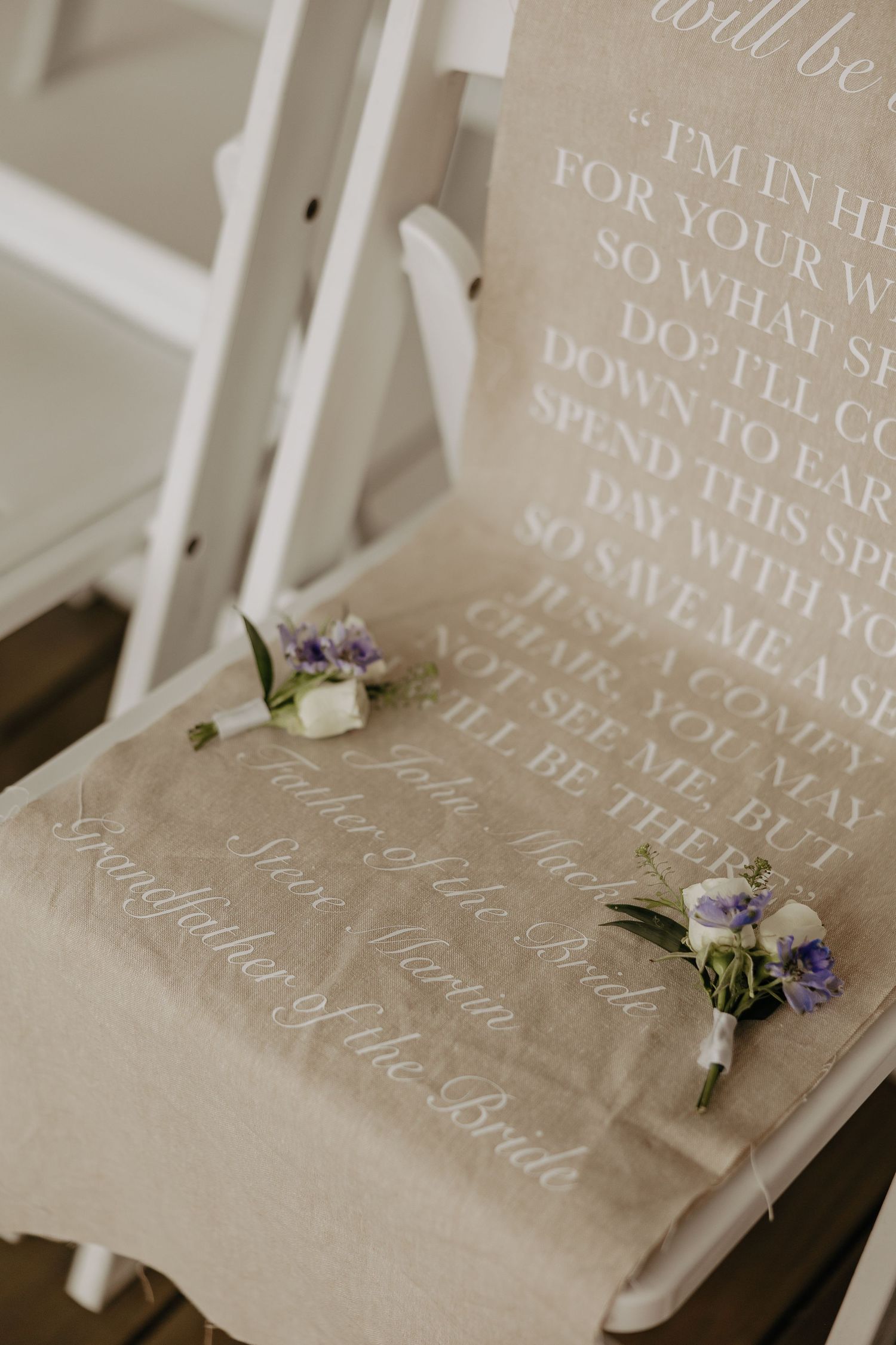 Wedding boutonnieres rest on a chair with romantic text printed on linen fabric in elegant script.