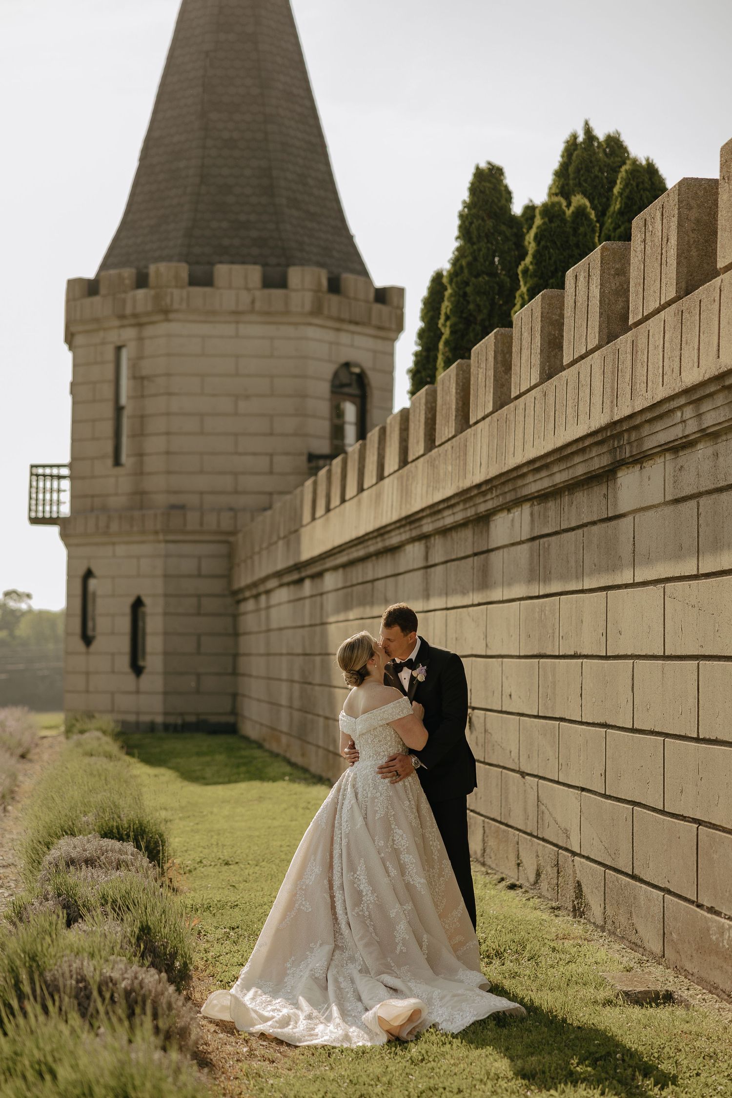 A romantic couple in wedding attire poses against a stone castle wall in a series of intimate portraits.