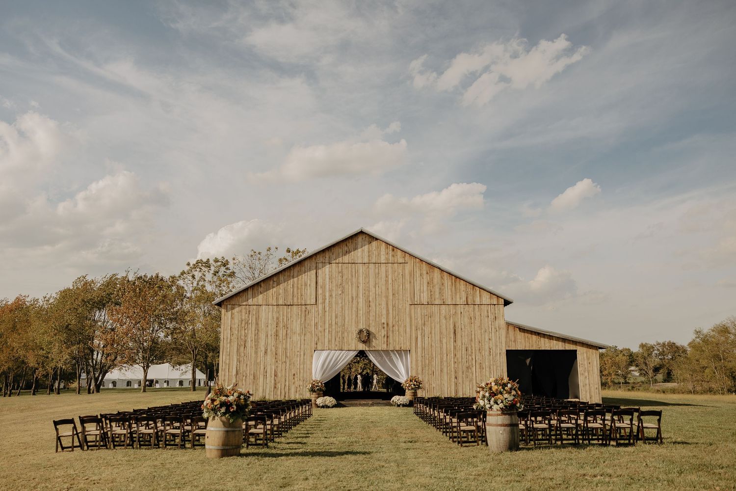 Rustic barn wedding venue panorama with wooden structure and outdoor ceremony setup.