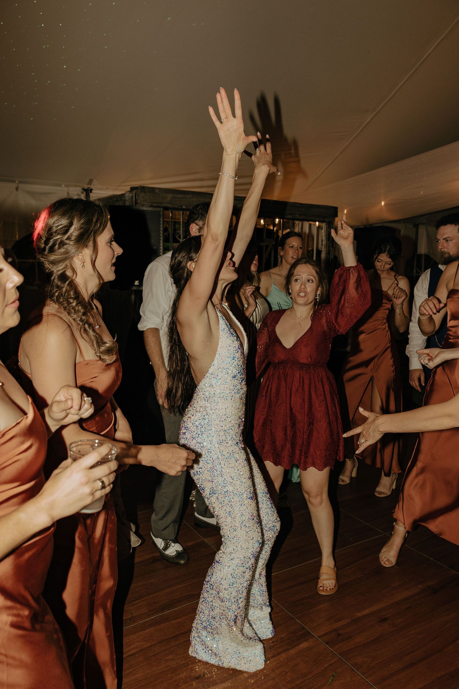 Wedding guests dancing energetically on a wooden dance floor at an evening reception.