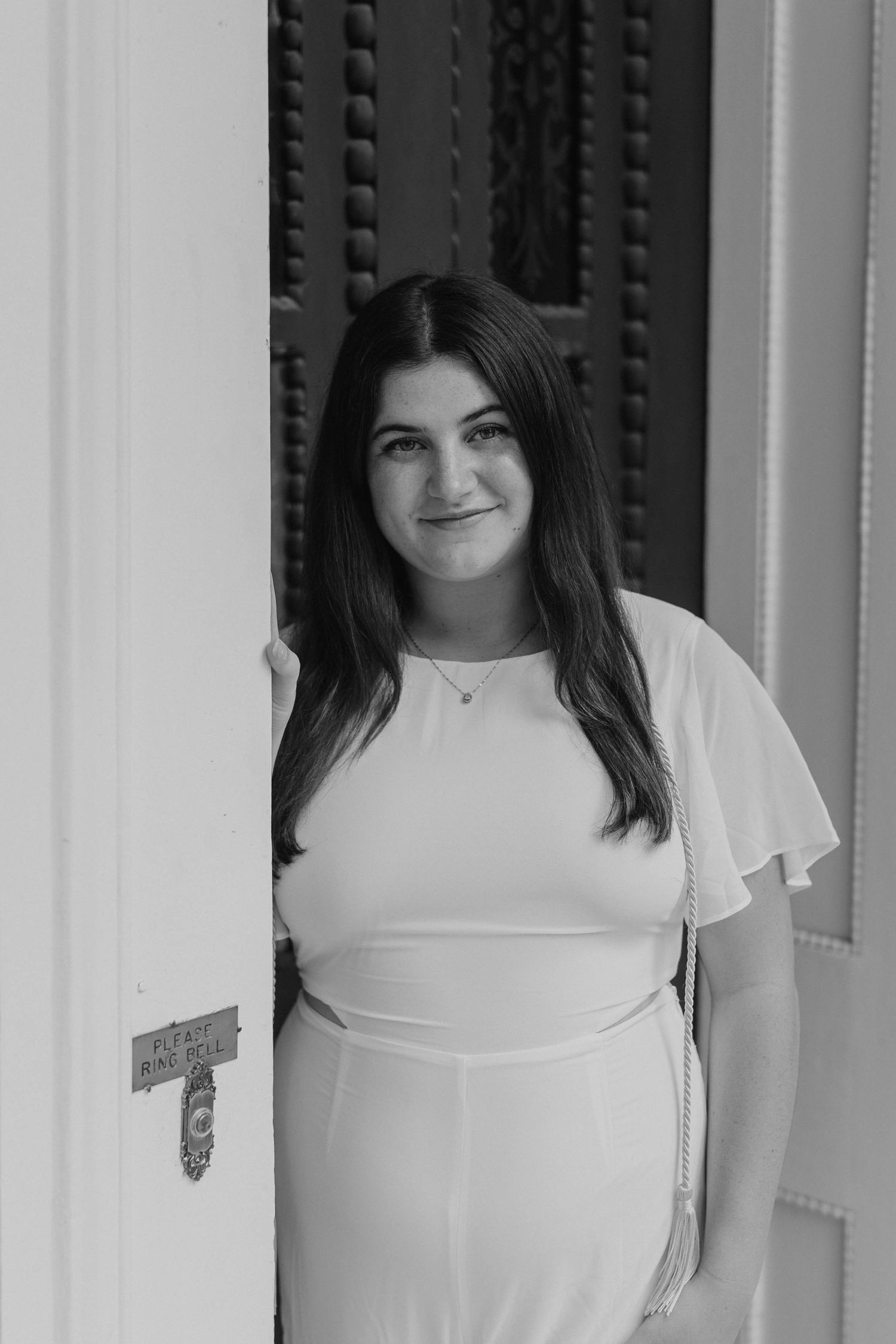 A black and white portrait taken between classical white columns of a historic building.