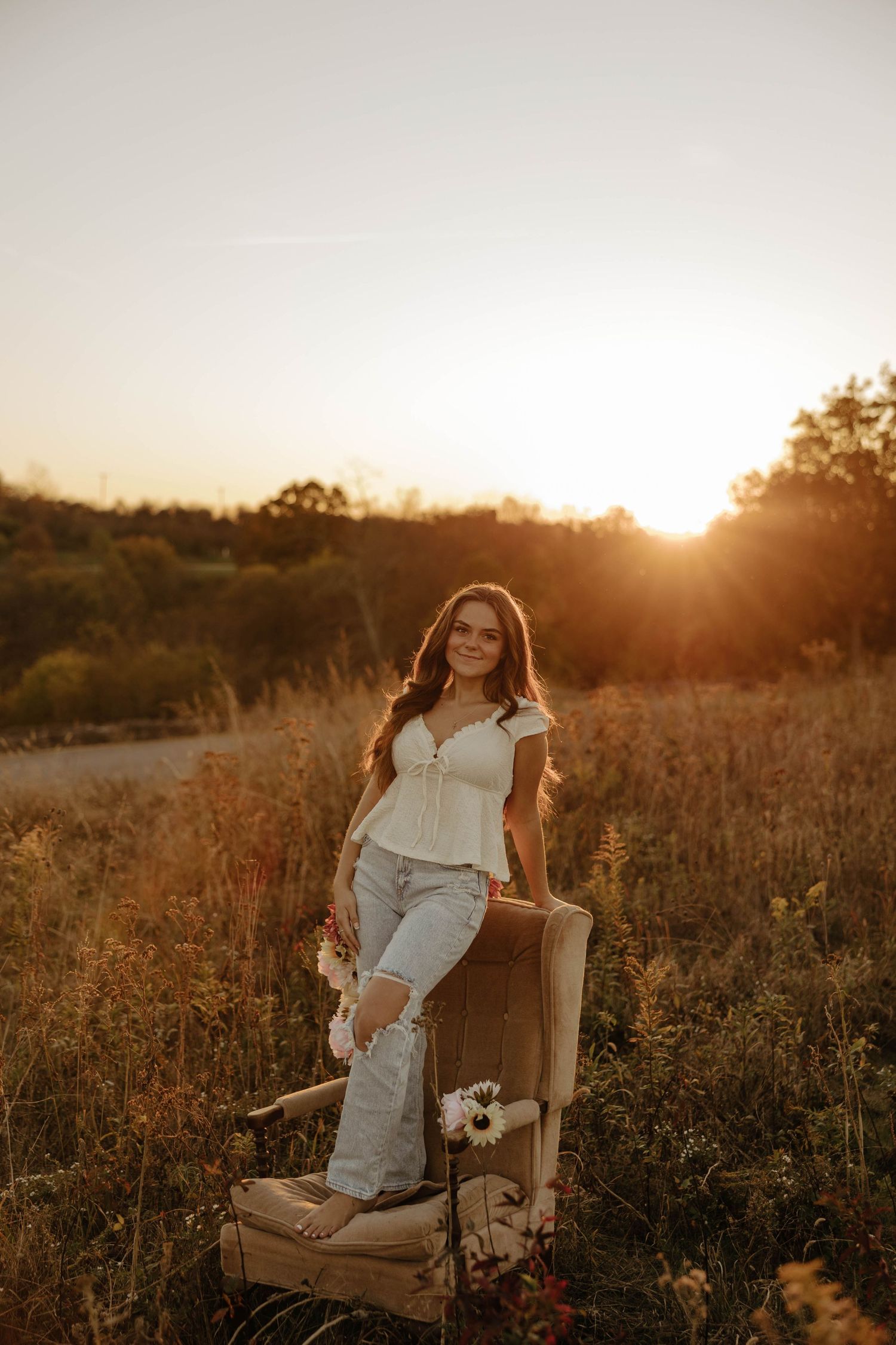 Artistic outdoor photoshoot at sunset featuring a vintage chair in a wildflower meadow.