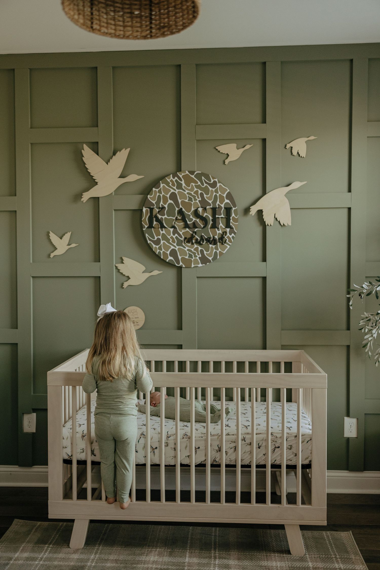 Modern nursery with sage green paneled walls decorated with white bird cutouts and a white crib.