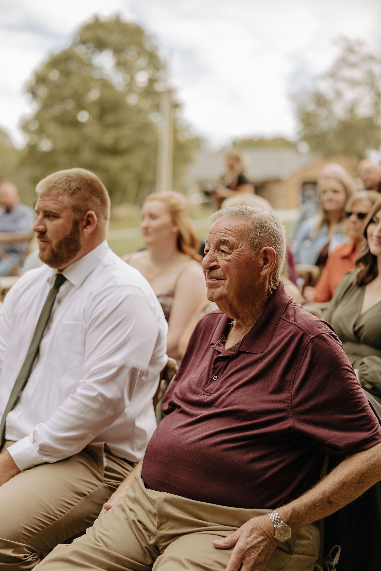 Wedding guests seated outdoors watching ceremony proceedings.