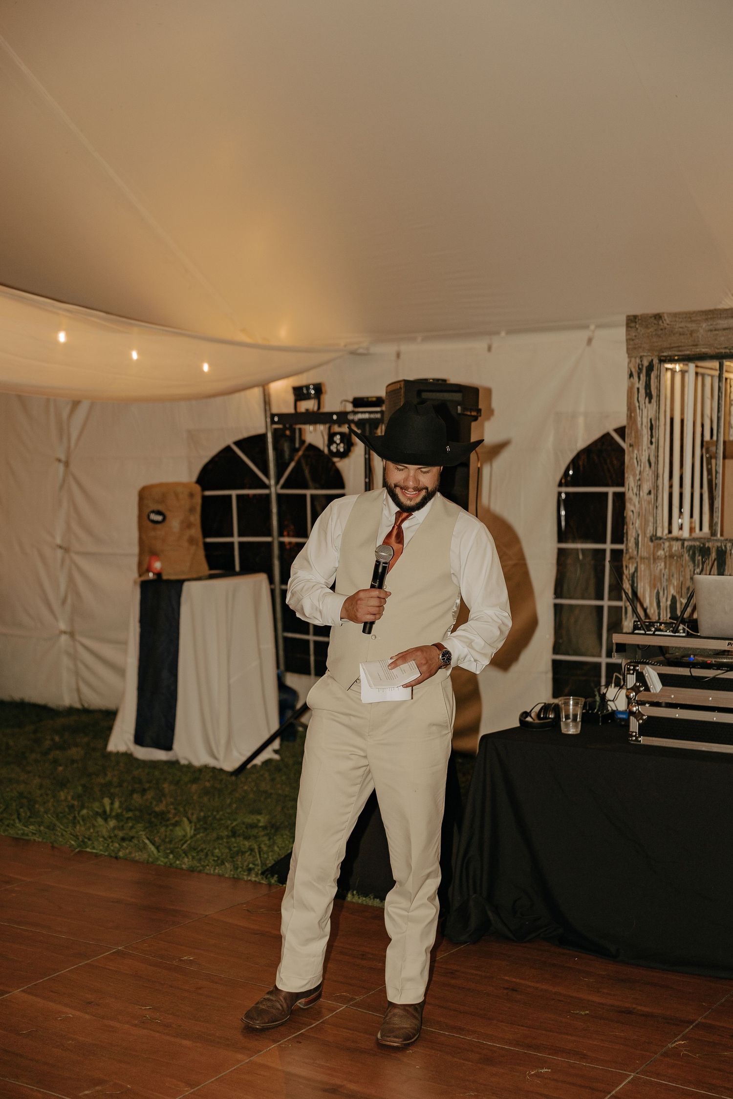 Wedding guests in white outfits dance on a wooden floor under a reception tent.